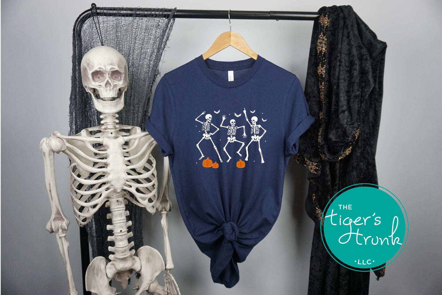 Navy blue t-shirt with skeleton design hanging on a rack next to a skeleton model, with 'The Tiger's Trunk' logo.