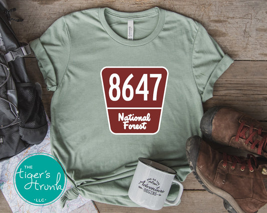 T-shirt with 8647 on a National Forest-style sign, earthy and subtle political protest design for nature lovers