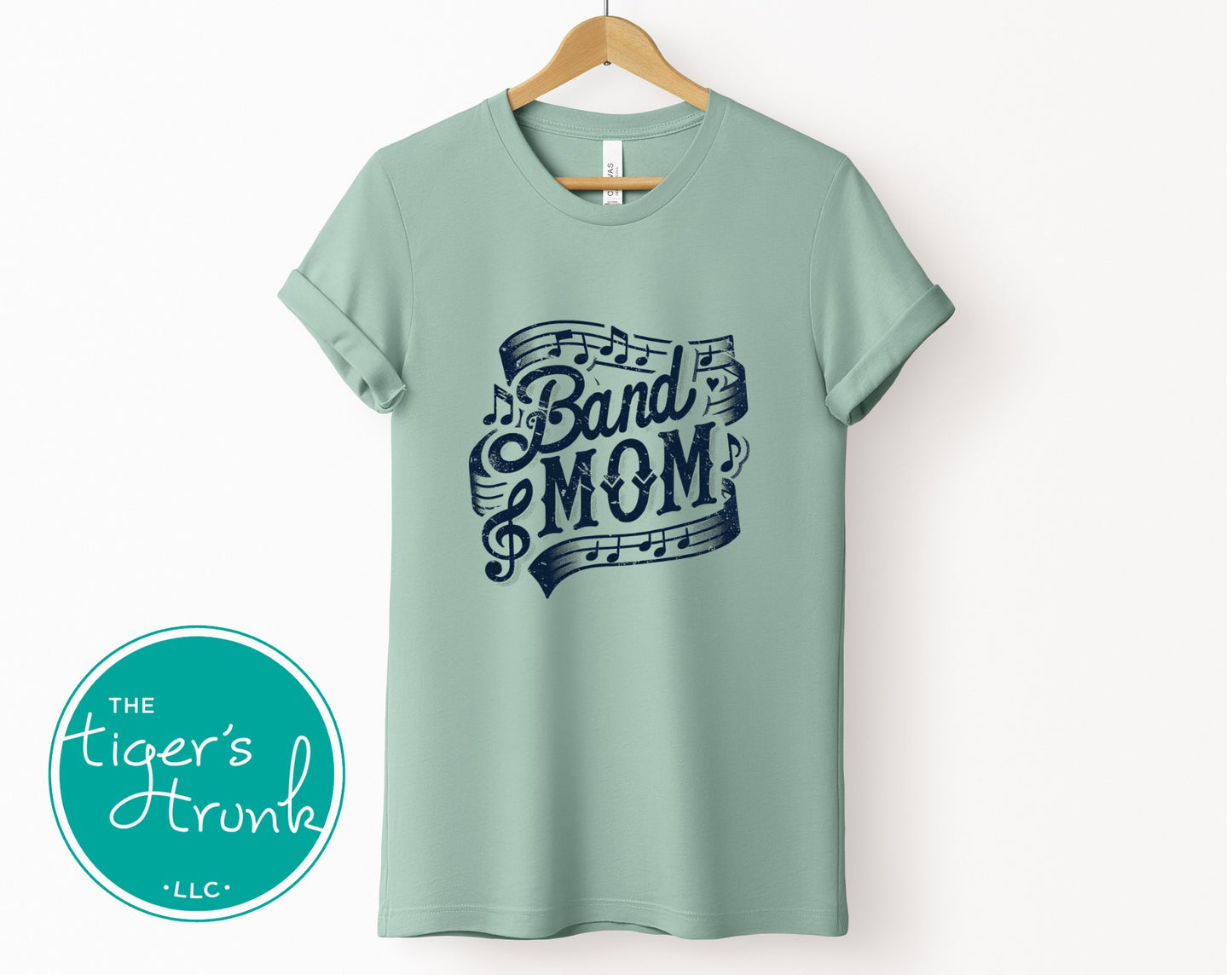 Light green t-shirt with 'Band Mom' design on a hanger, featuring The Tiger's Trunk logo.