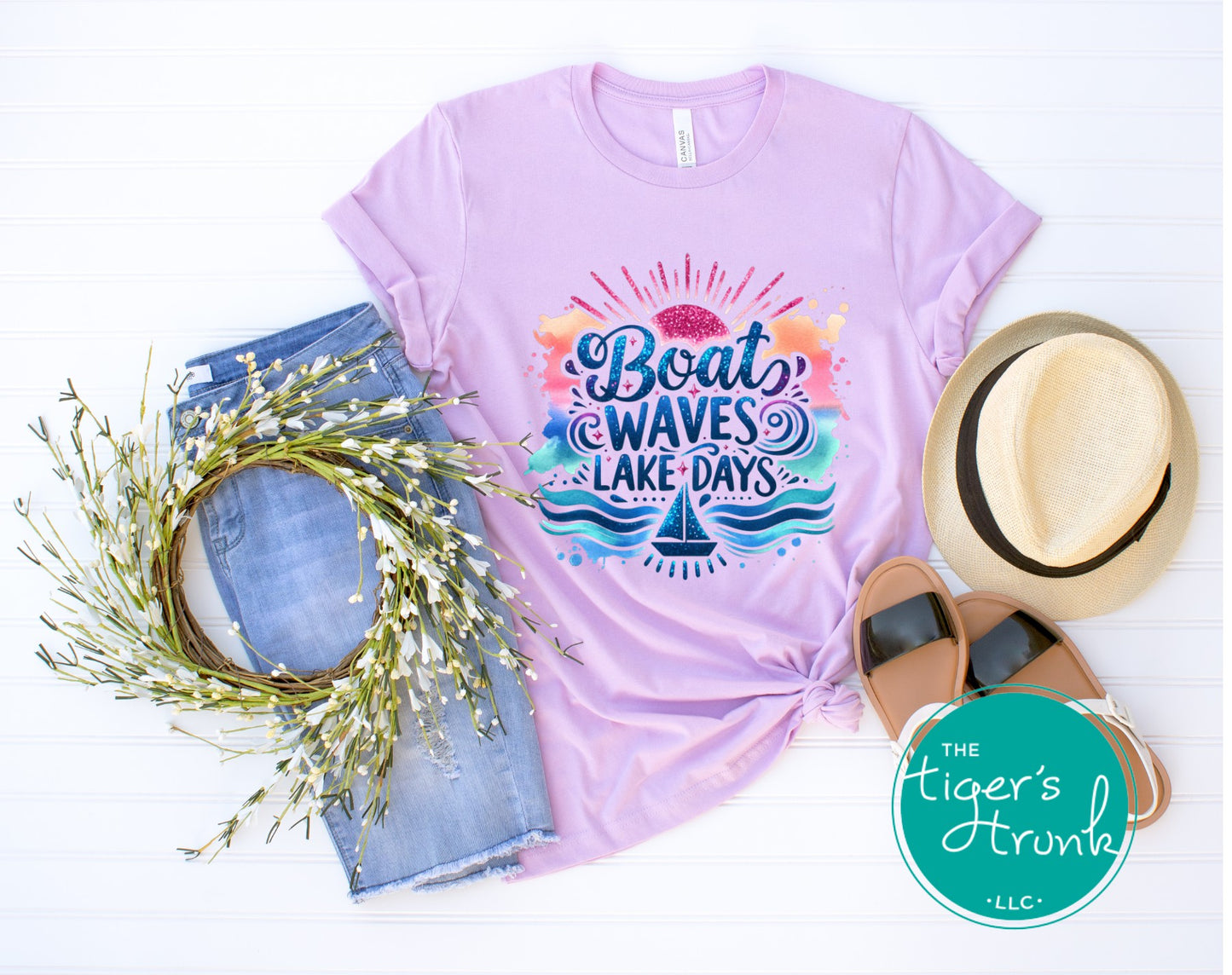 Lavender t-shirt with 'Boat Waves Lake Days' design, jeans, sandals, and a hat on a white background.