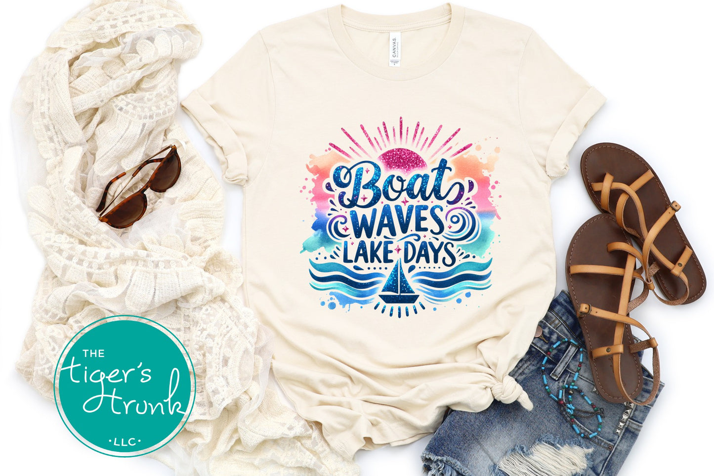 Beige t-shirt with 'Boat Waves Lake Days' design, scarf, sunglasses, and sandals on a white background.
