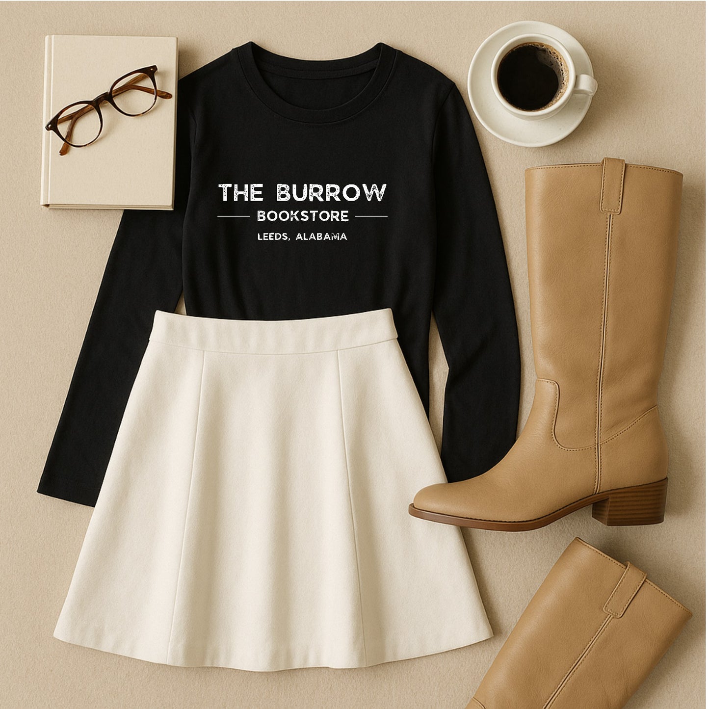 Black shirt with 'The Burrow Bookstore' text, white skirt, tan boots, book, glasses, and coffee cup on a beige surface.