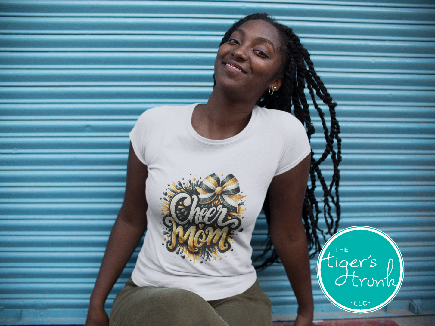 Woman wearing a 'Cheer Mom' t-shirt in front of a blue shutter, with 'The Tiger's Trunk' logo.