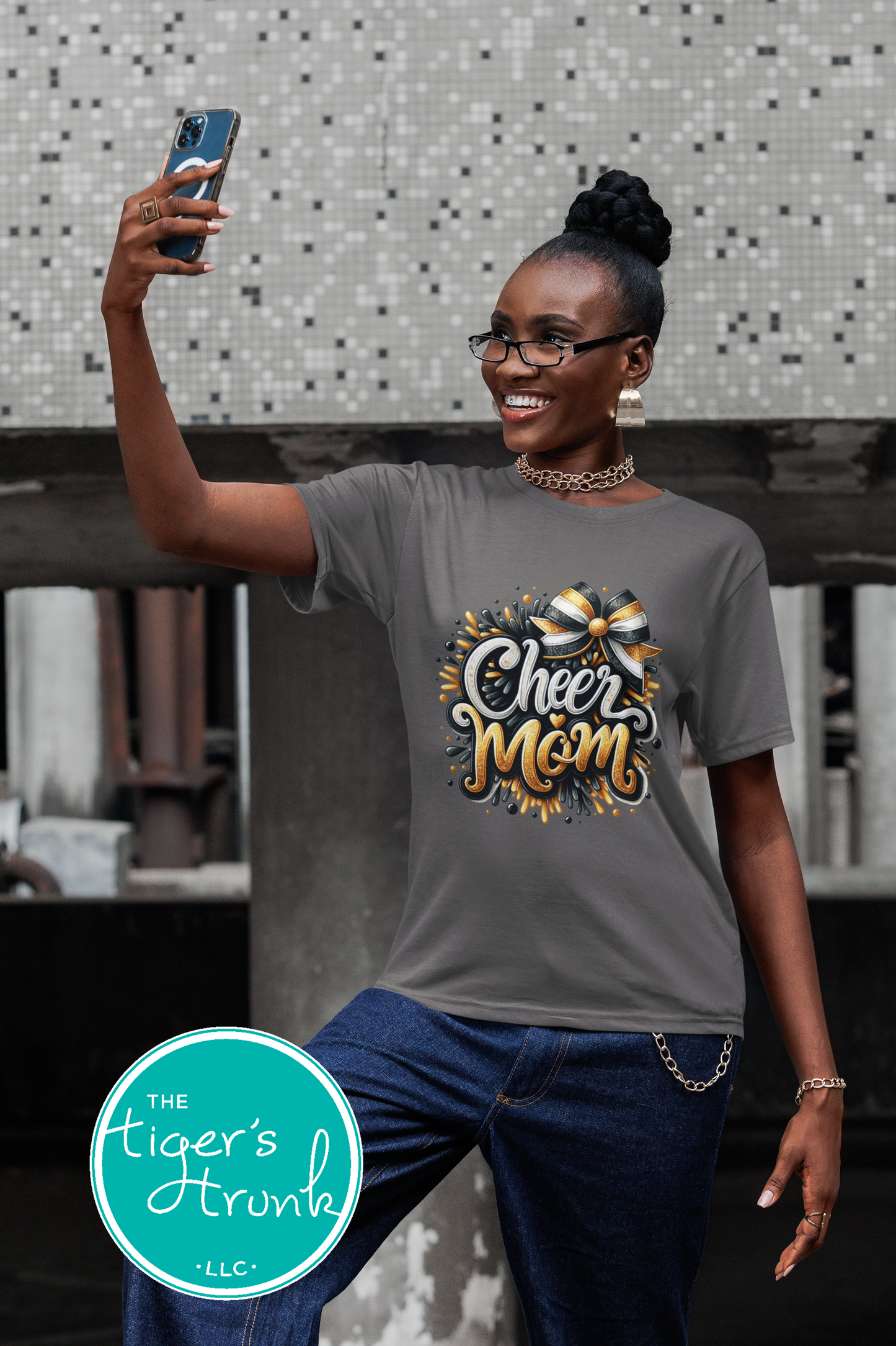 Woman taking a selfie wearing a 'Cheer Mom' t-shirt with a decorative design.