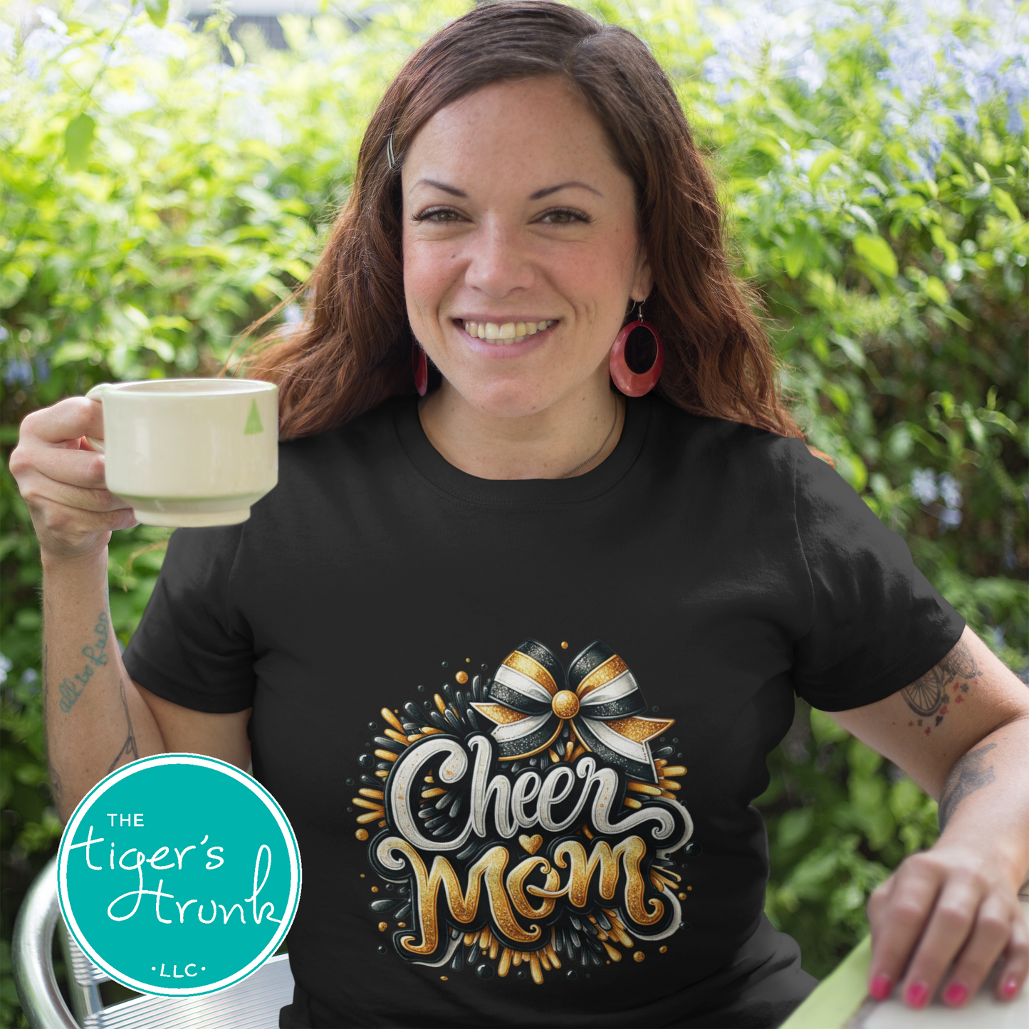 Woman wearing a black t-shirt with 'Cheer Mom' design, holding a mug outdoors.