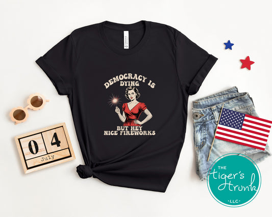 Funny political t-shirt that reads Democracy Is Dying But Hey, Nice Fireworks, worn for sarcastic July Fourth cookouts