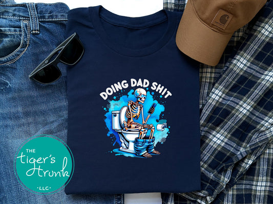 Skeleton sitting on a toilet with the phrase "Doing Dad Shit," printed on a t-shirt for dad humor and Father’s Day gifts