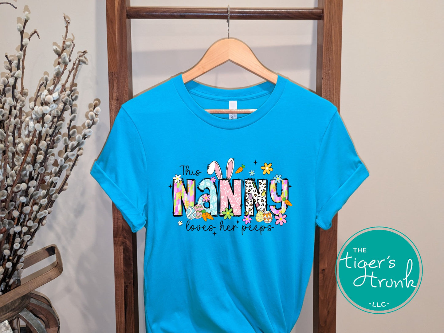 Easter t-shirt with "Nanny" in spring print font decorated with bunnies, eggs, and flowers, perfect for holiday wear and springtime fun