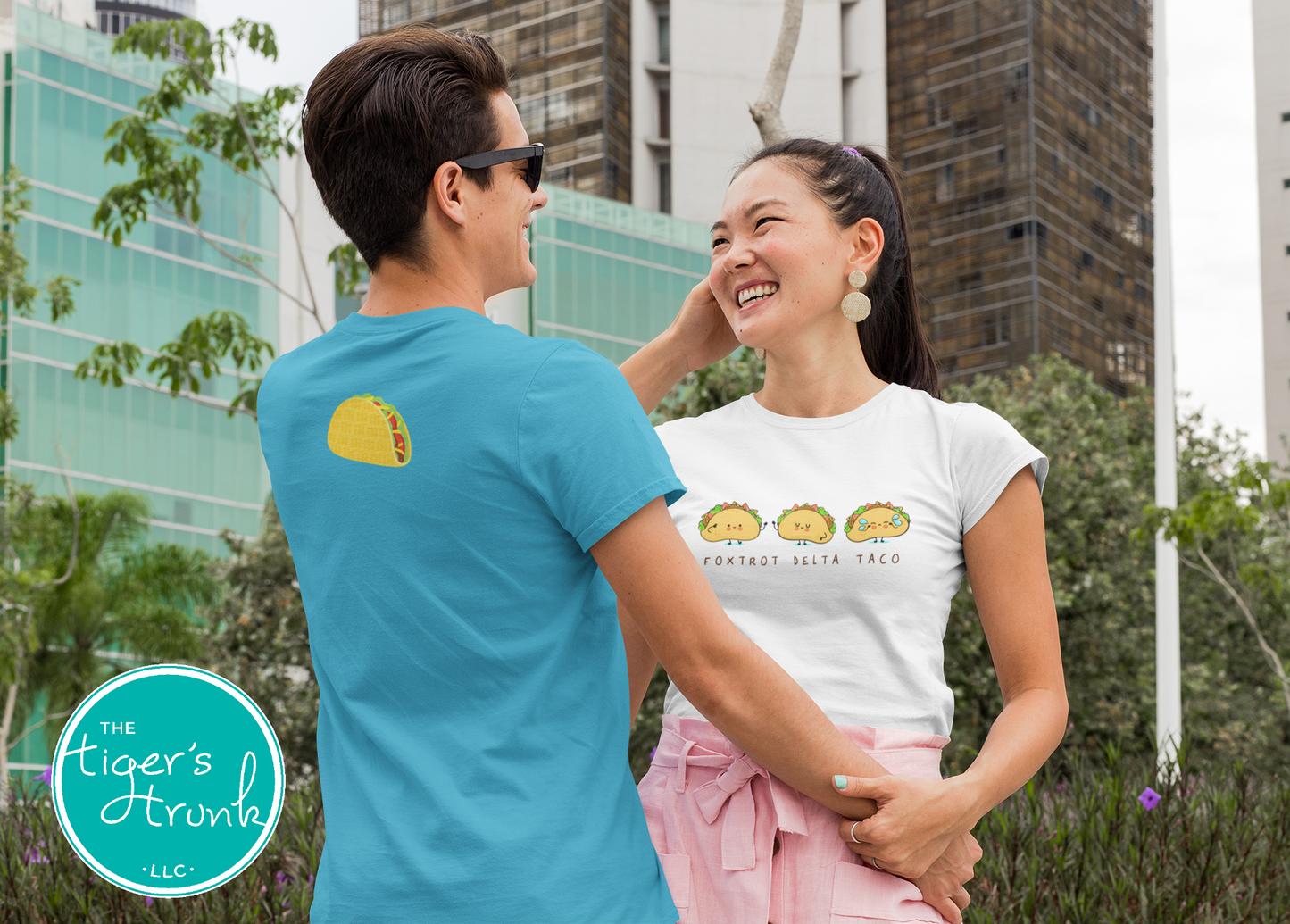 Two people wearing t-shirts with brand logos, standing outdoors with a cityscape background.