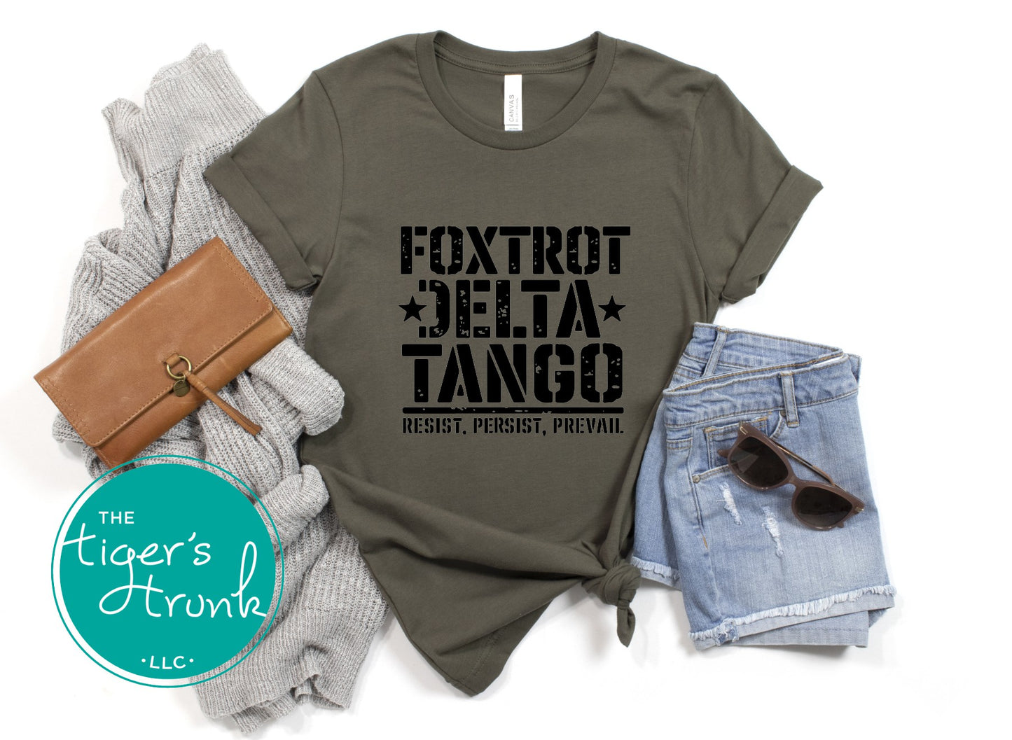 Olive green t-shirt with 'Foxtrot Delta Tango' text, paired with a brown wallet, gray sweater, denim shorts, and sunglasses on a white background.