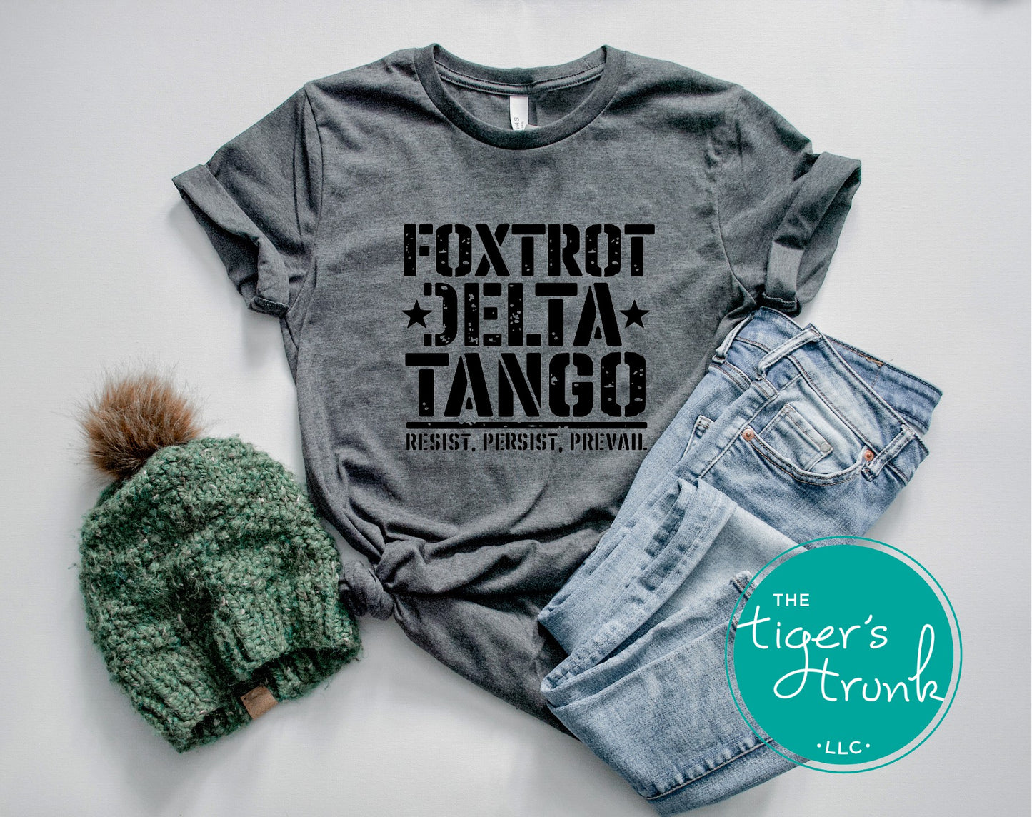 Gray t-shirt with 'Foxtrot Delta Tango' text, green beanie, and denim shorts on a light gray background.