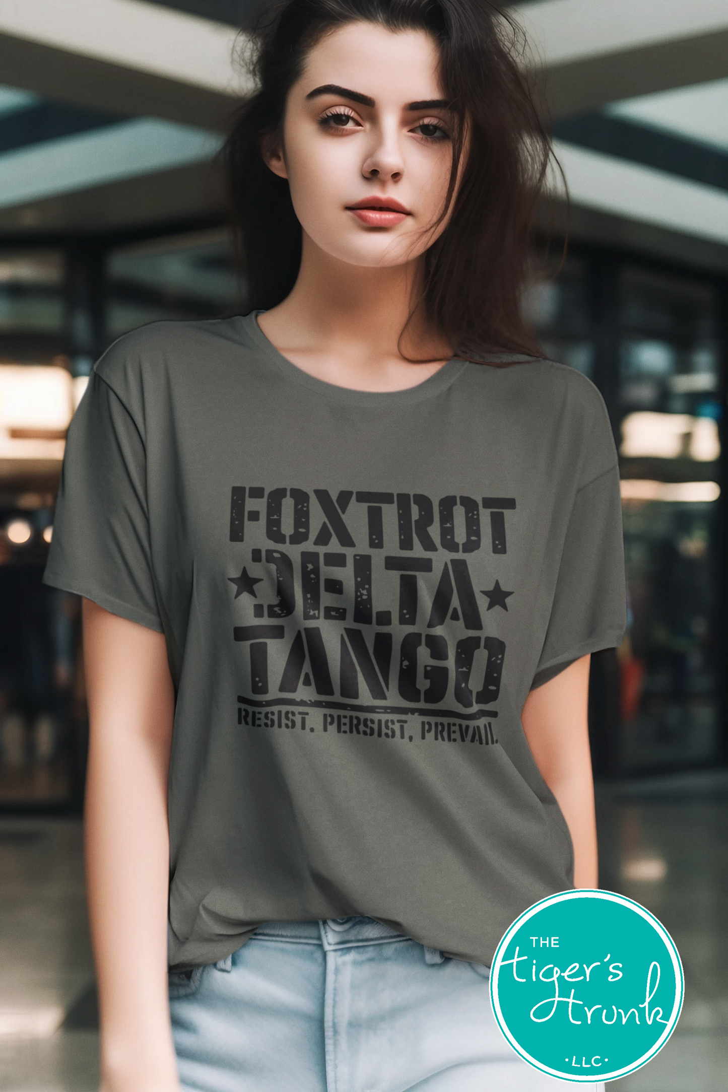 Woman wearing a gray t-shirt with 'Foxtrot Delta Tango' text, standing in an indoor setting.