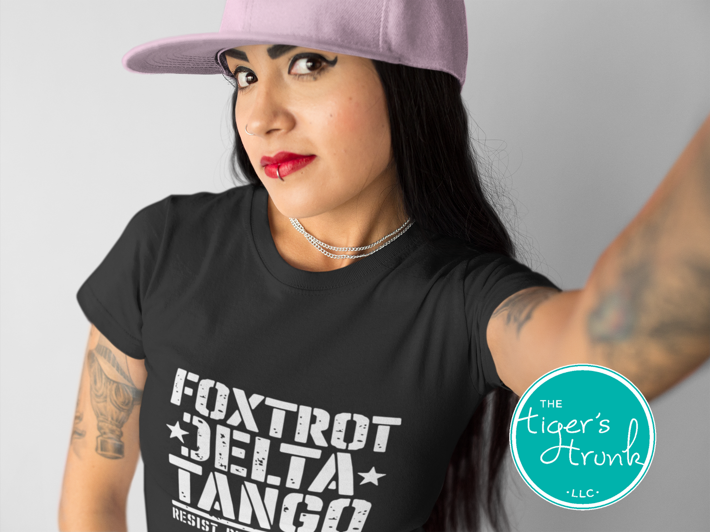Woman wearing a black t-shirt with 'Foxtrot Delta Tango' text and a pink cap, with 'The Tiger's Trivio' logo.