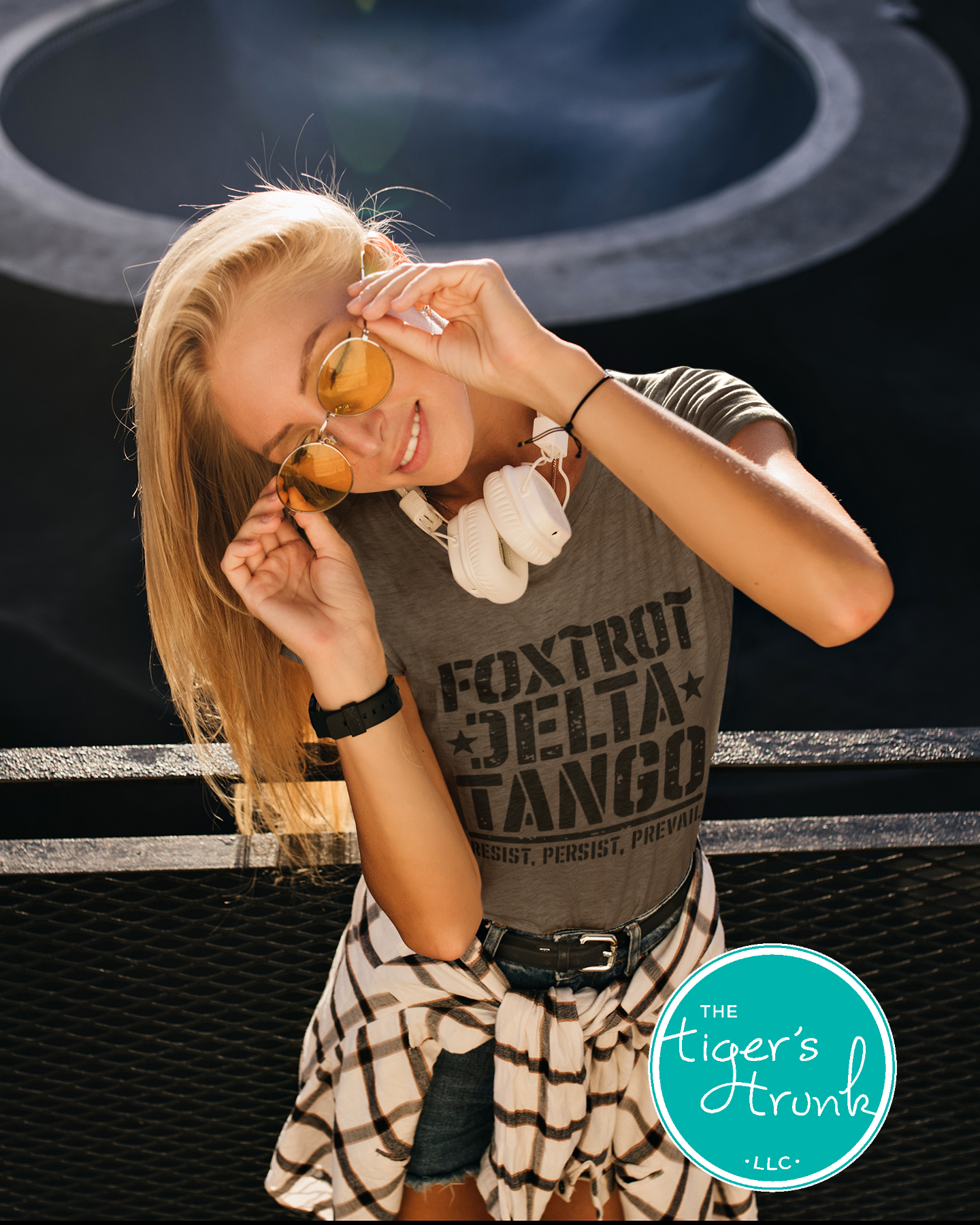 Woman wearing a 'Foxtrot Delta Tango' shirt with sunglasses, standing against a dark background.