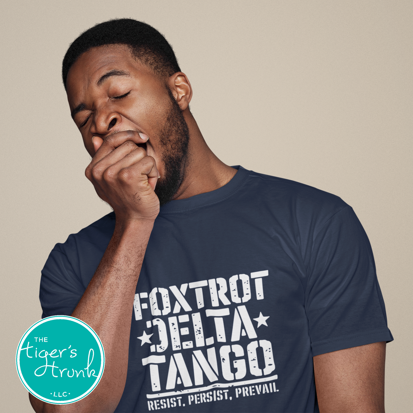 Man wearing a navy blue t-shirt with 'Foxtrot Delta Tango' text, yawning against a beige background.