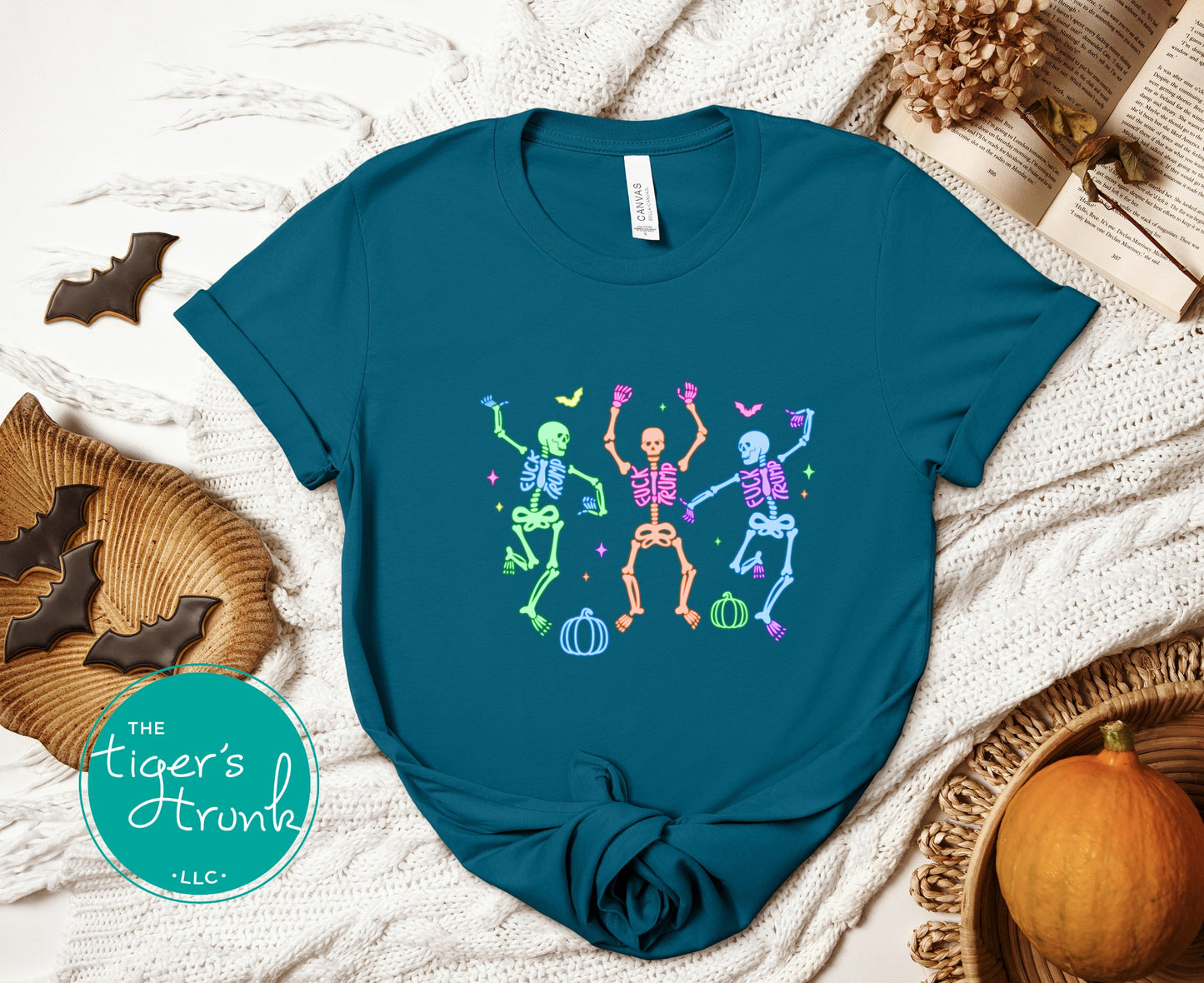 Blue t-shirt with colorful skeleton design on a textured surface with Halloween decorations.