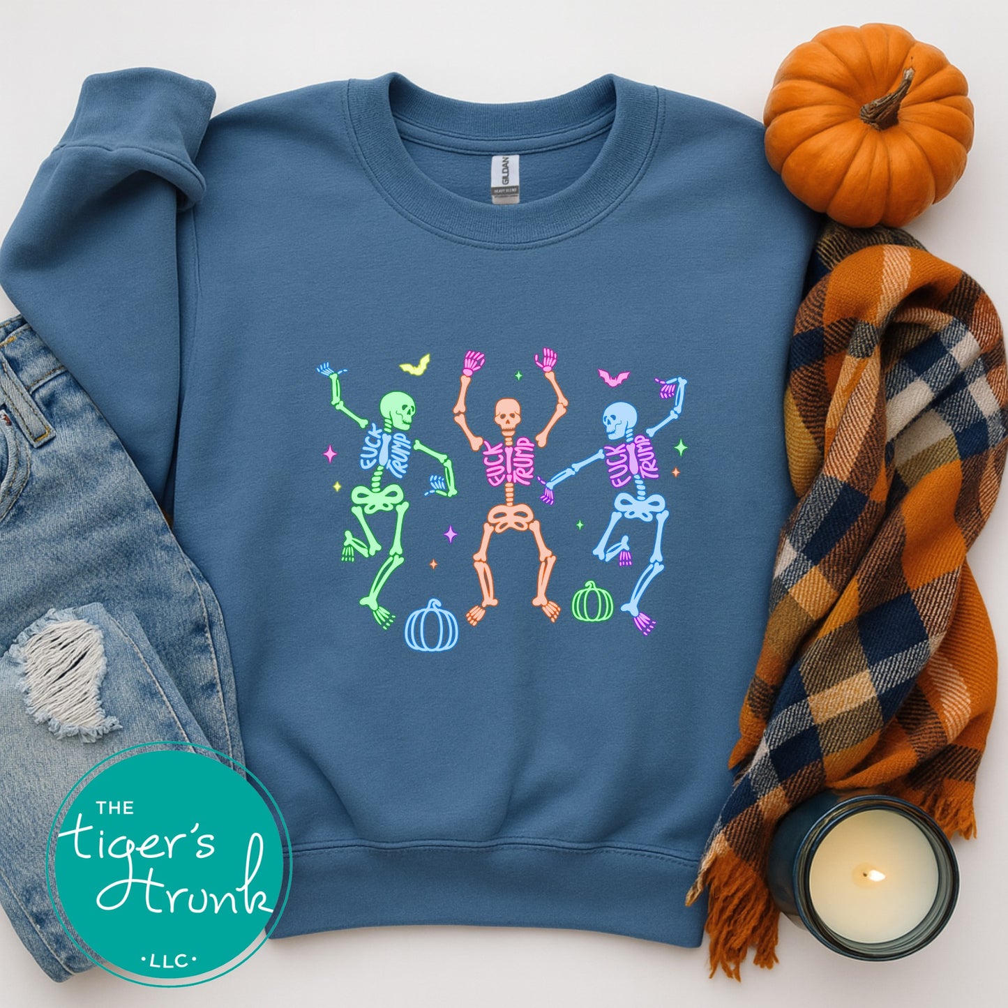 Blue sweatshirt with colorful skeleton design, surrounded by jeans, a plaid scarf, and a pumpkin on a white background.