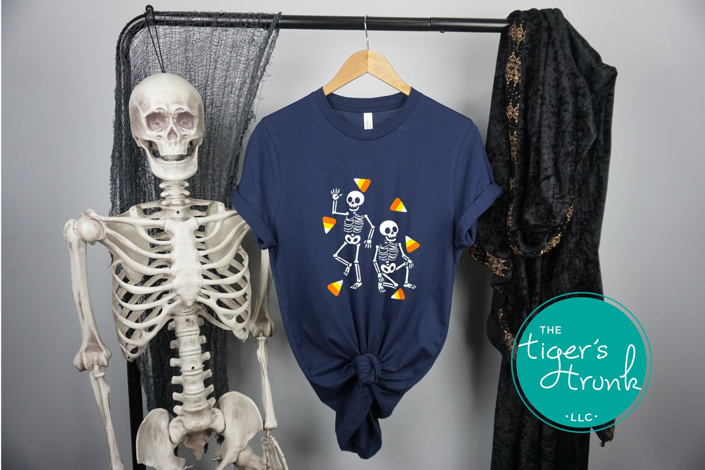 Navy blue t-shirt with skeleton design on a hanger next to a skeleton model, with 'The Tiger's Trunk' logo.