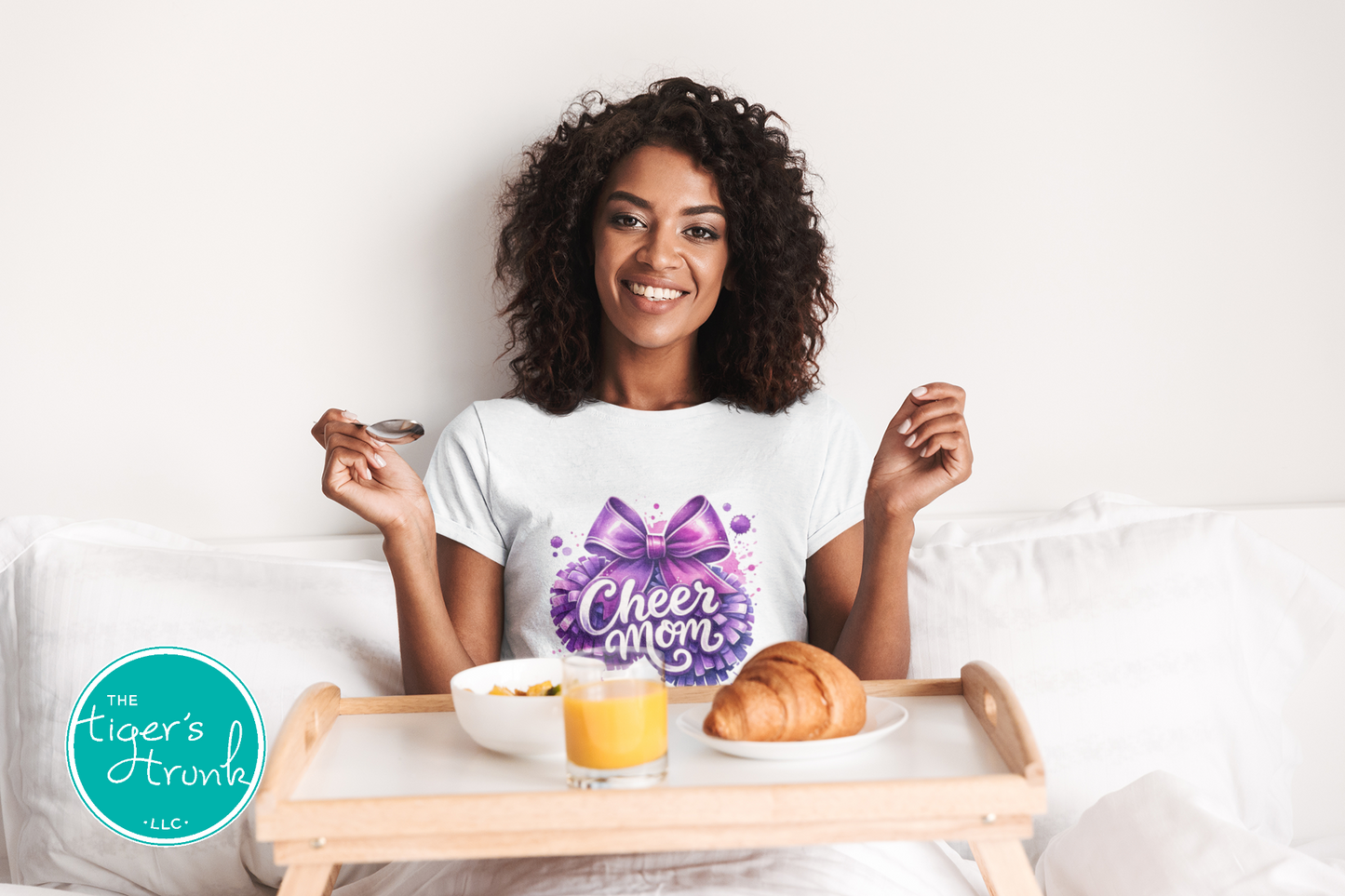 Woman in a white t-shirt with a purple bow design, sitting in bed with a tray of food.