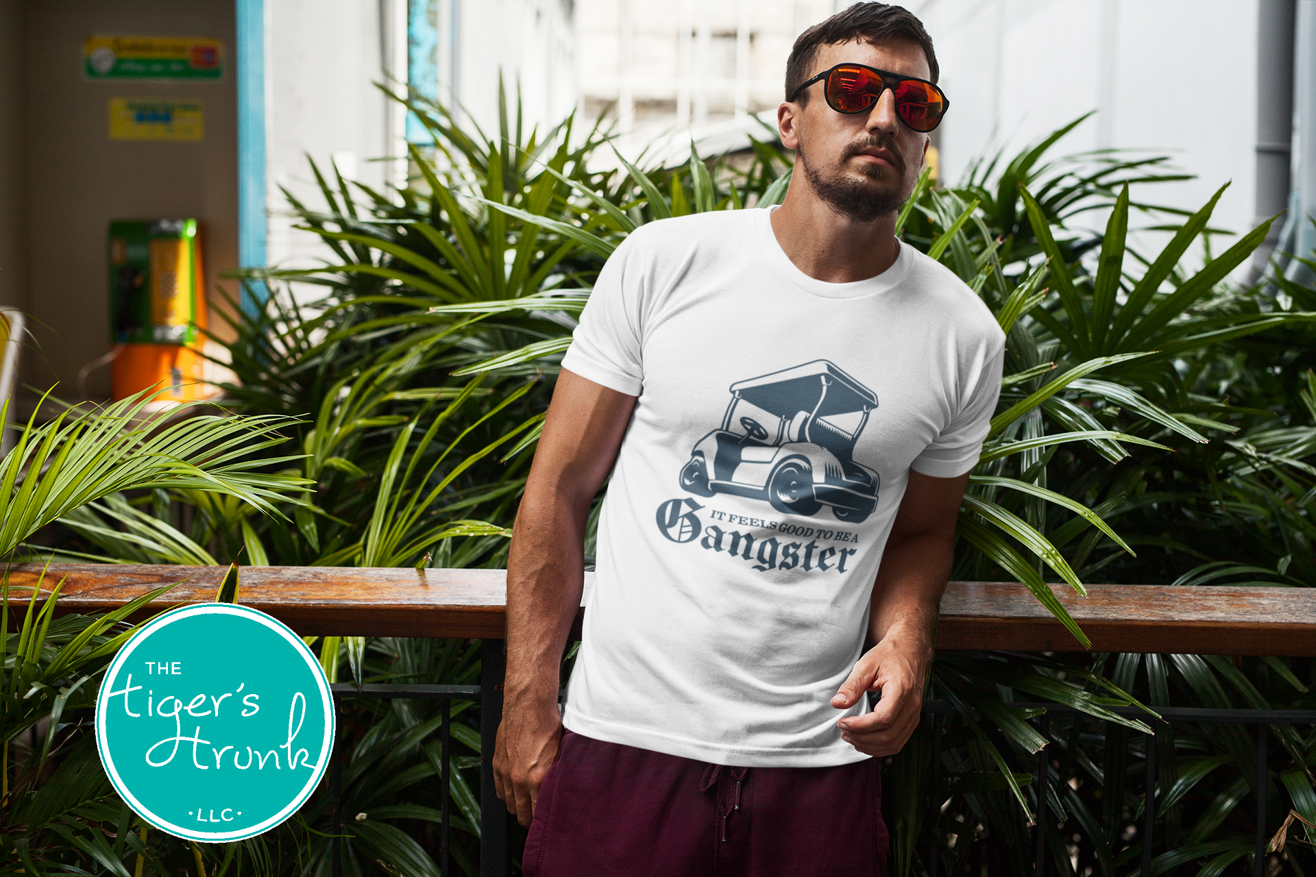Male model wearing white golf cart shirt with navy graphic that says It Feels Good to Be a Gangster, funny golf tee for men, gift for golfer