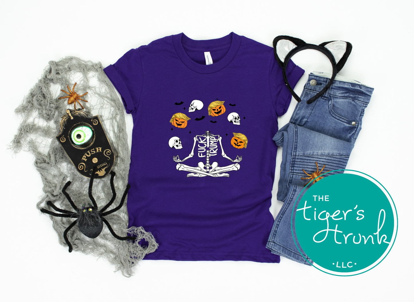 Purple t-shirt with Halloween design, jeans, and decorative items on a white background with 'The Tiger's Trunk' logo.