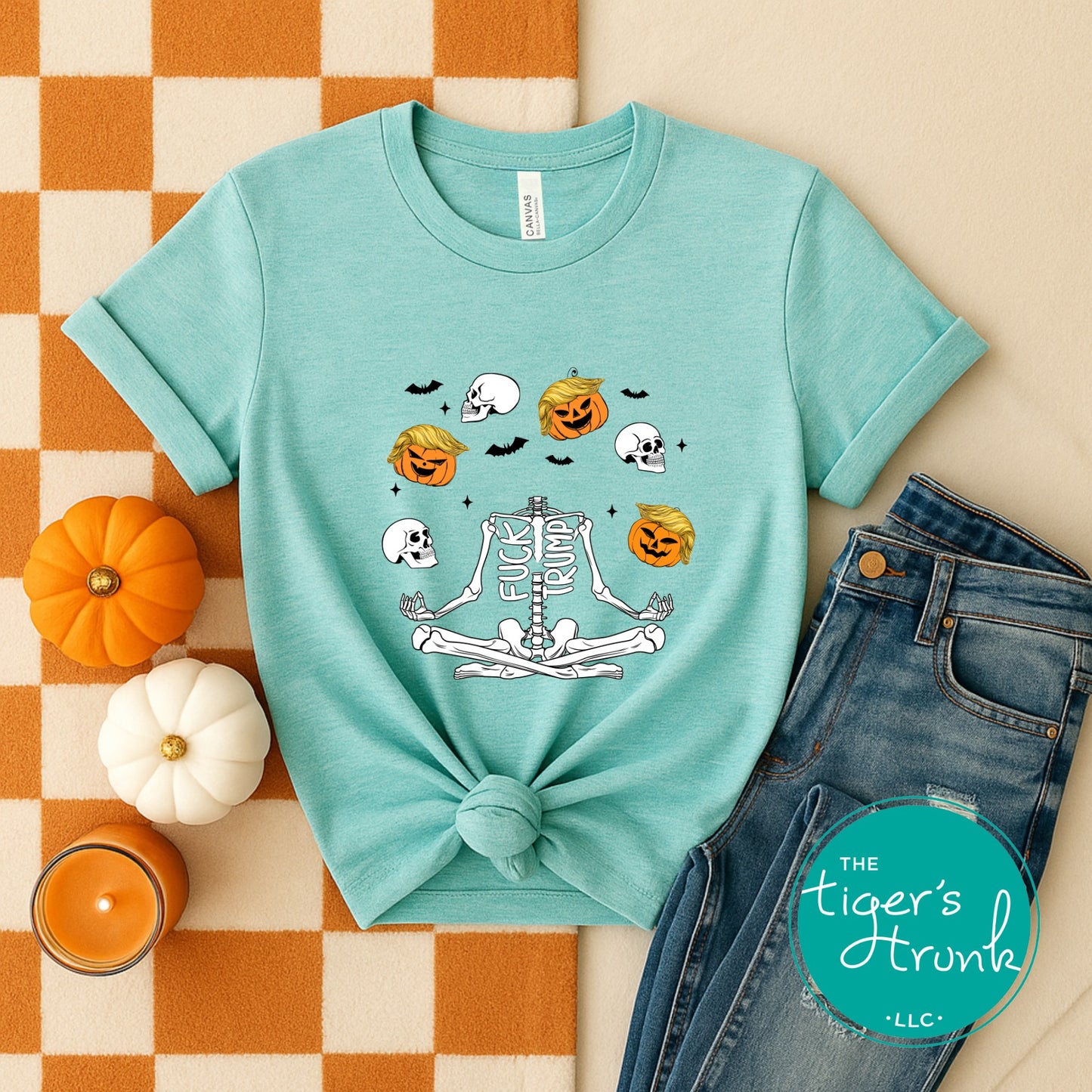 Teal t-shirt with Halloween-themed design on a checkered tablecloth with pumpkins and jeans.