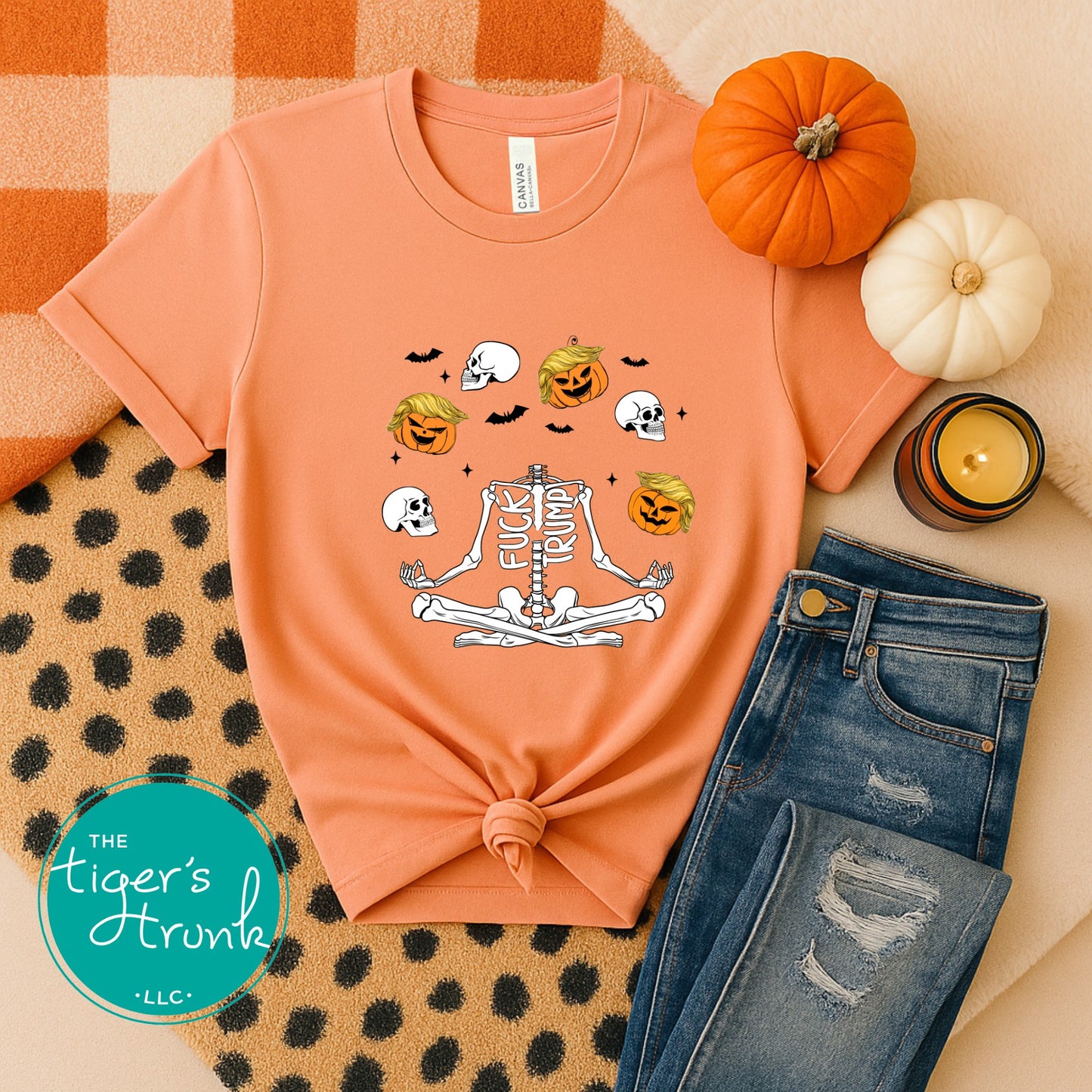 Orange t-shirt with graphic design, jeans, pumpkins, and candle on a patterned surface.
