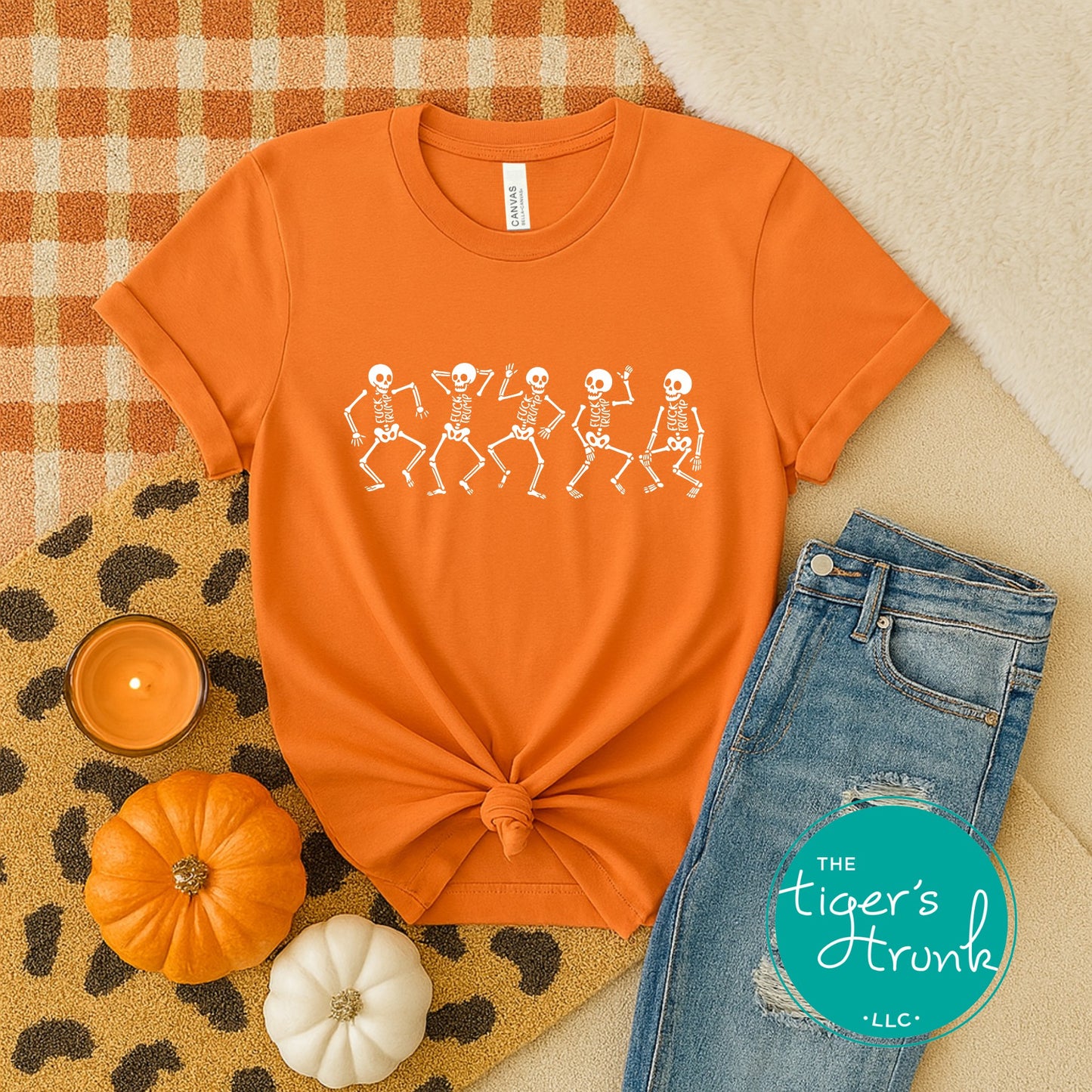 Orange t-shirt with skeleton design, jeans, pumpkins, and candle on a checkered fabric background.