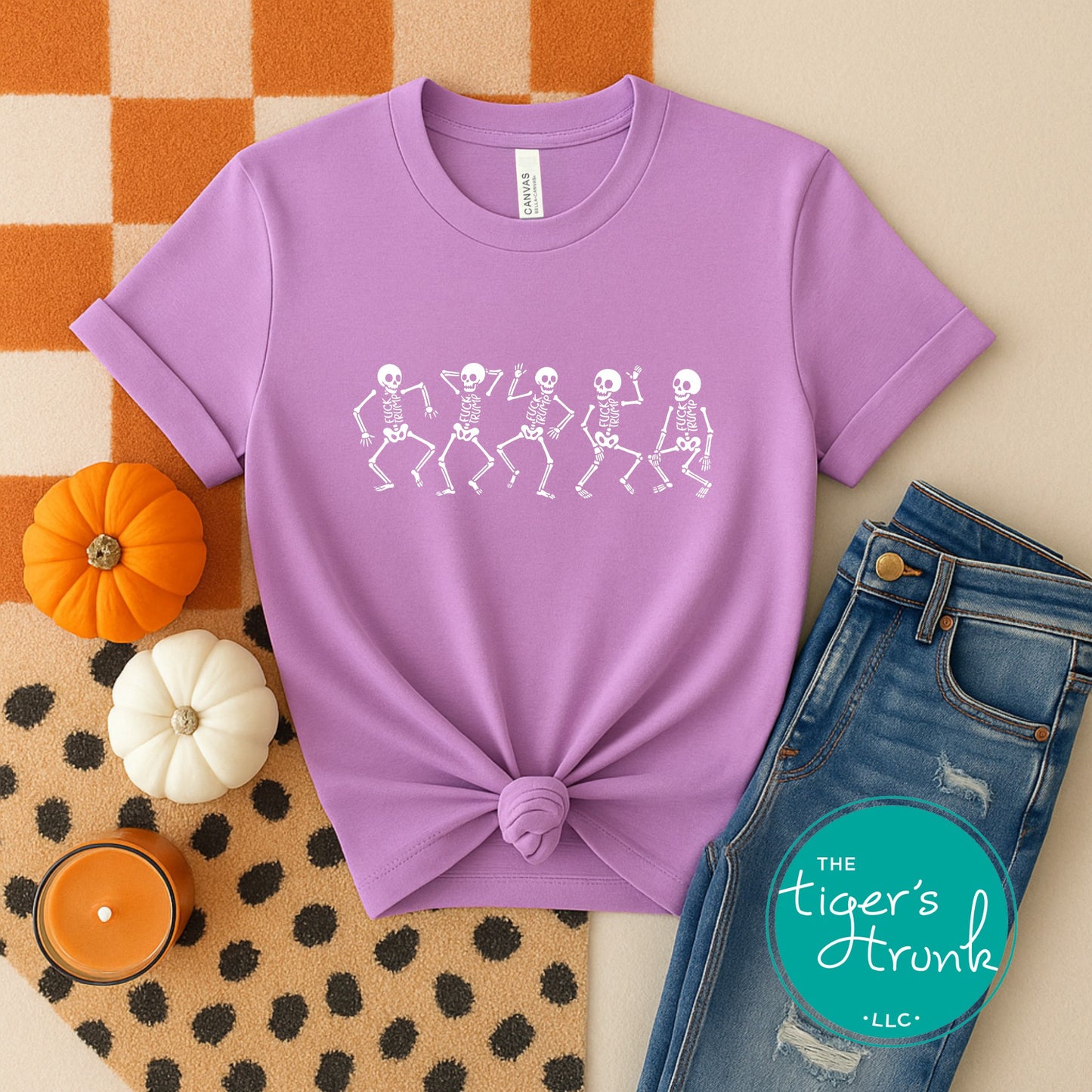 Purple t-shirt with skeleton design, jeans, and pumpkins on a patterned surface with 'The Tiger's Trunk' logo.