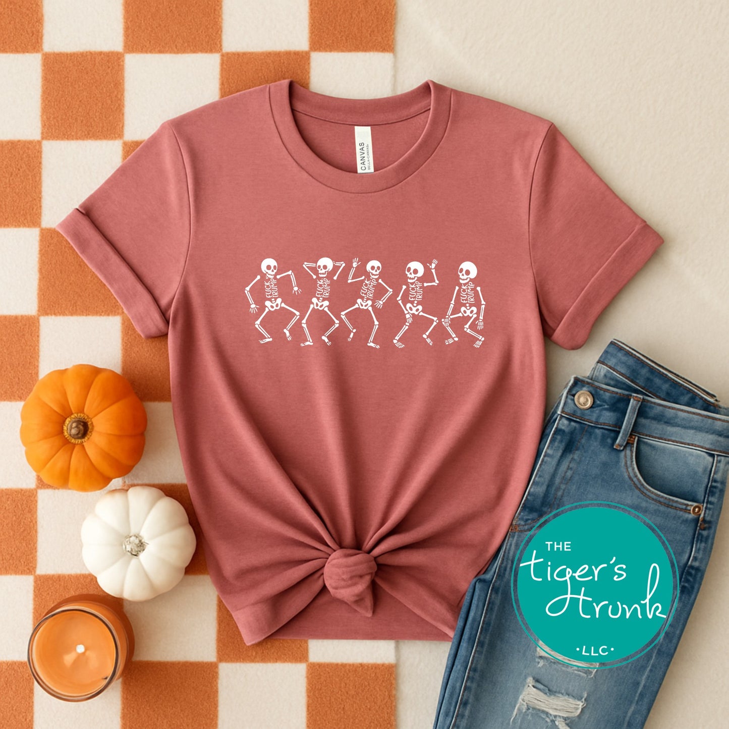 Pink t-shirt with skeleton design, jeans, pumpkins, and candle on a checkered background
