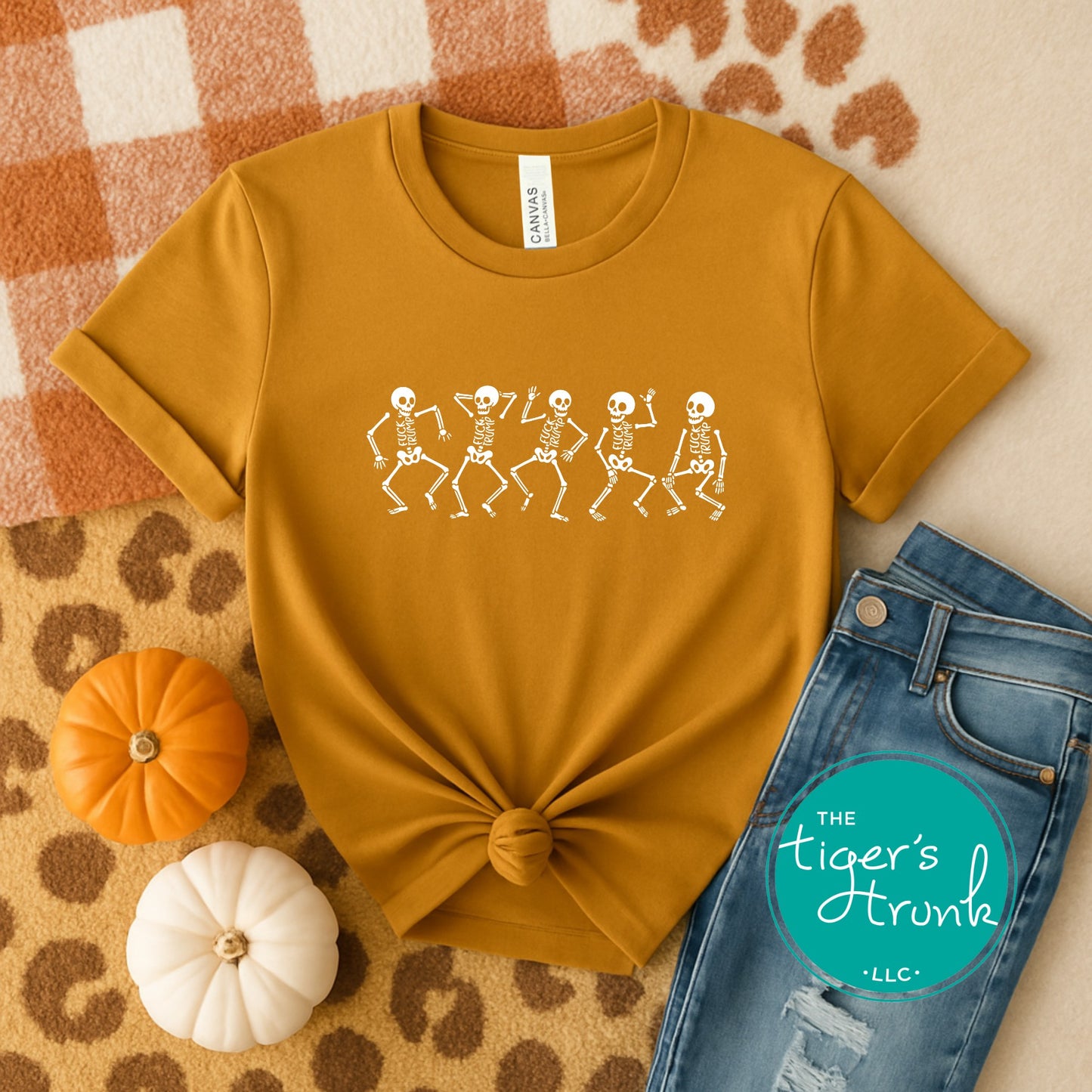 Mustard yellow t-shirt with skeleton design on a patterned surface with pumpkins and jeans.
