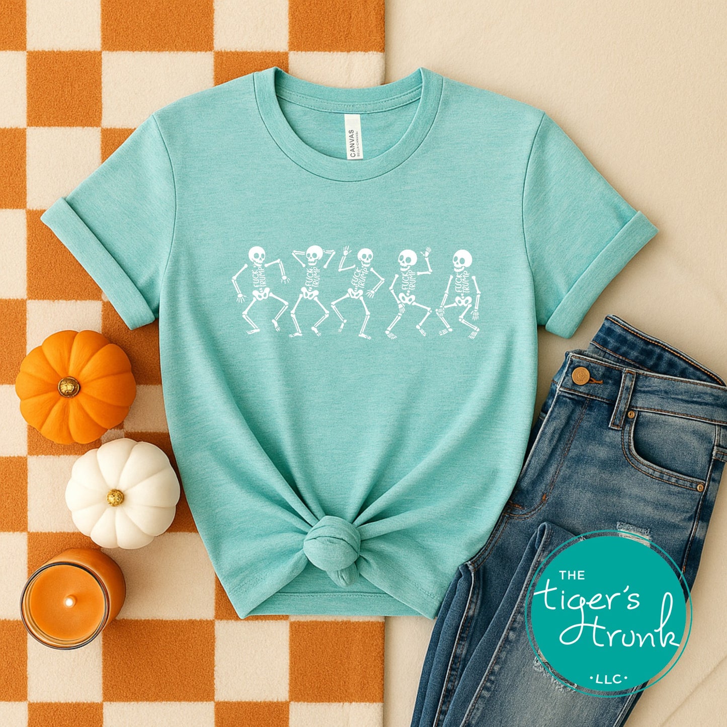 Teal t-shirt with skeleton design, jeans, pumpkins, and candle on a checkered surface with 'The Tiger's Horn' logo.