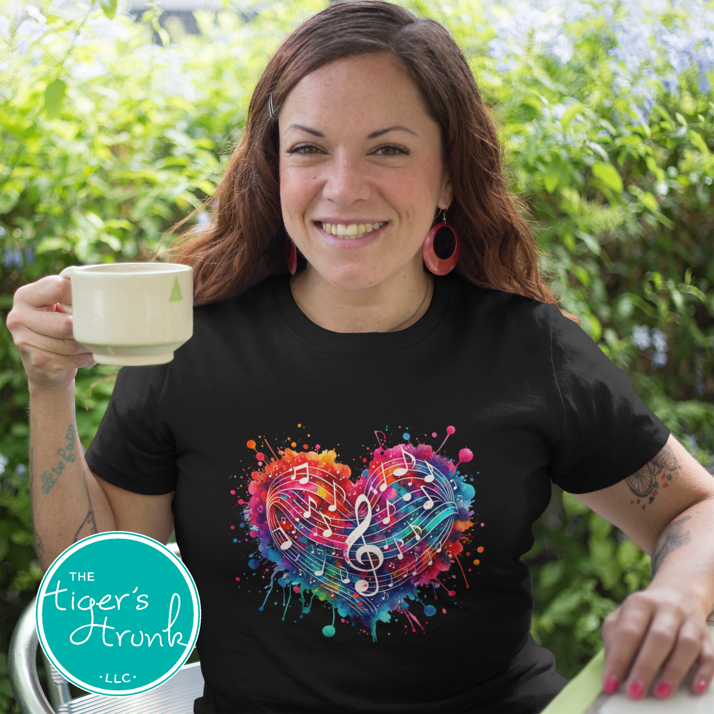 Woman wearing a black t-shirt with a colorful heart design holding a mug outdoors.