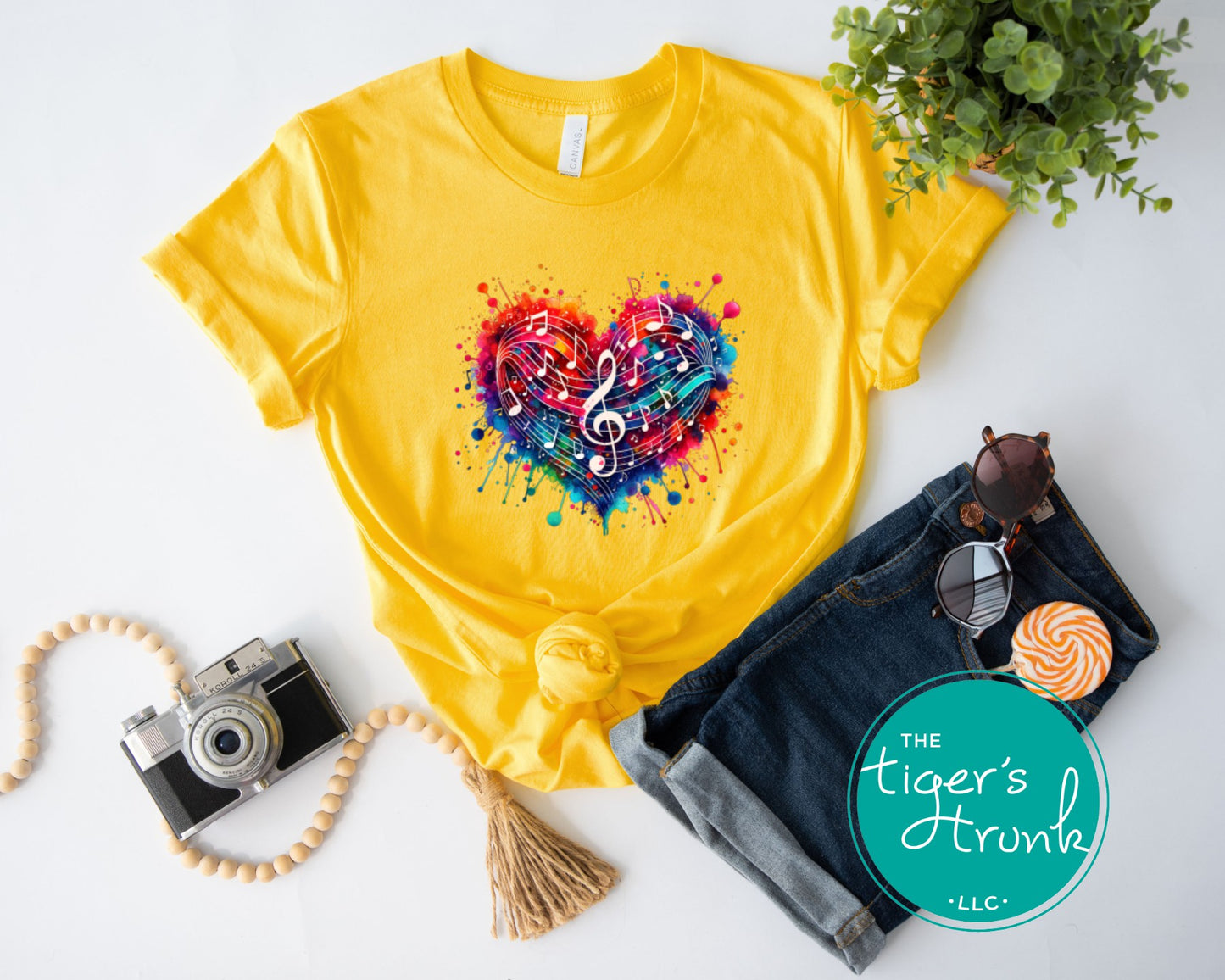 Yellow t-shirt with colorful heart design, camera, sunglasses, and jeans on a white background.