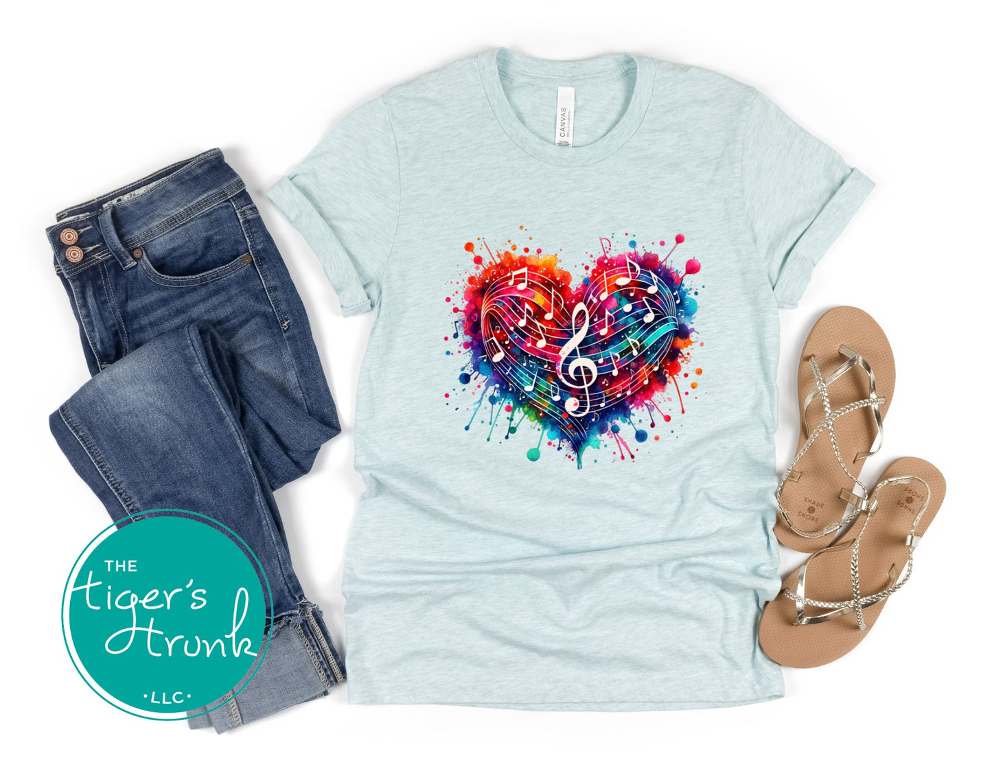 Light blue t-shirt with colorful heart design, jeans, and sandals on a white background with 'The Tiger's Trunk' logo.