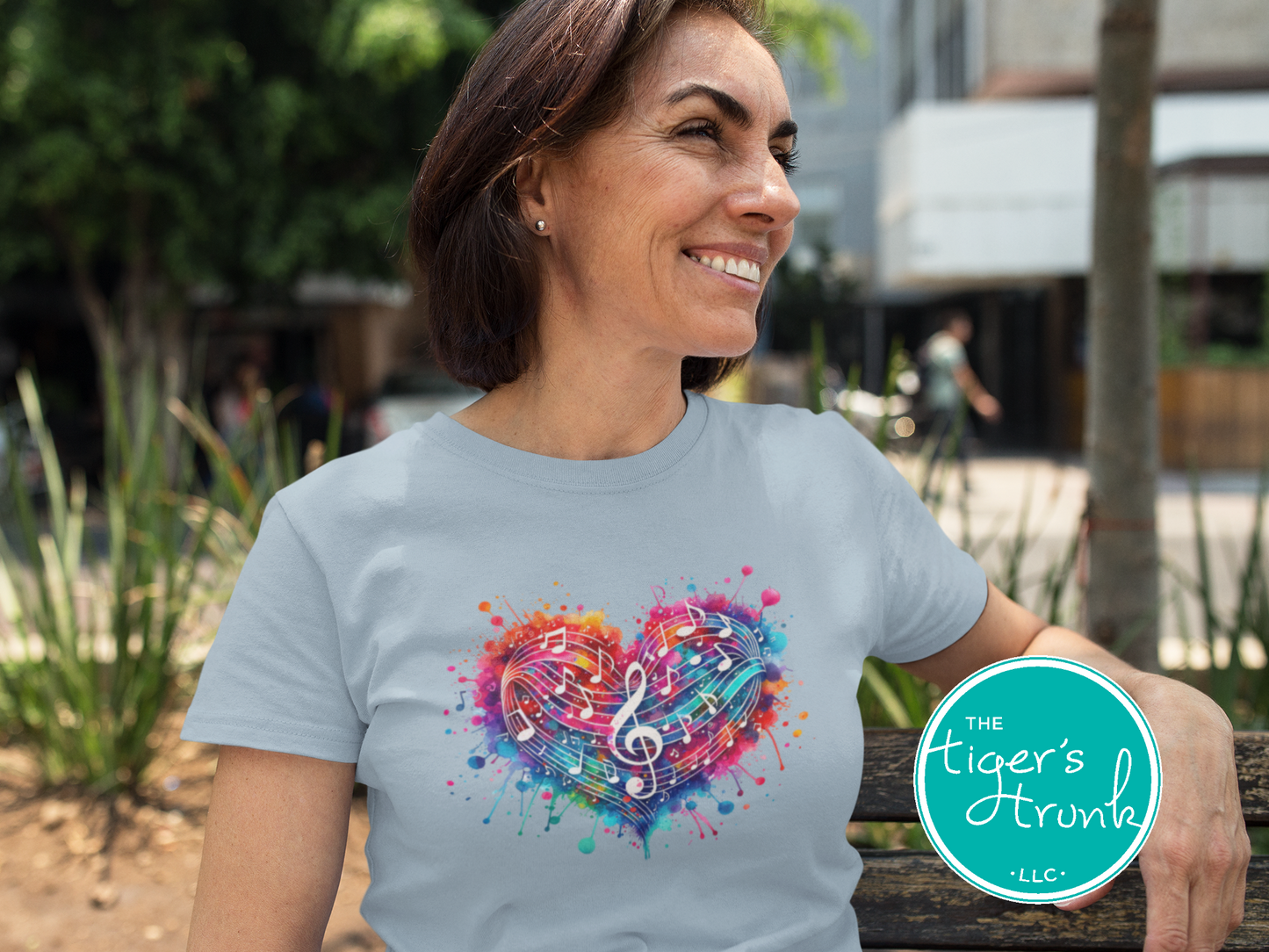 Woman wearing a light blue t-shirt with a colorful heart and music notes design, standing outdoors.