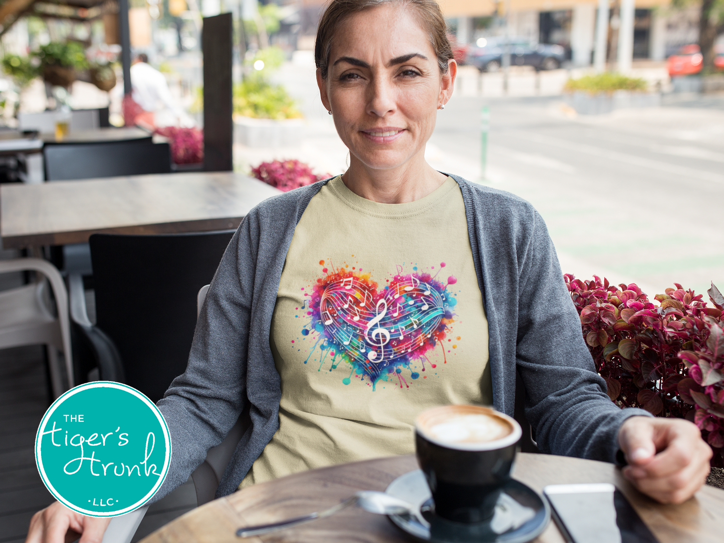 Woman wearing a colorful graphic t-shirt with a heart and musical notes design, sitting at an outdoor cafe.