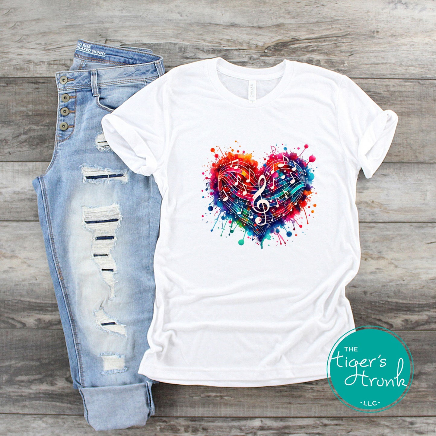 White t-shirt with colorful heart design and ripped jeans on a wooden surface, featuring 'The Tiger's Trunk' brand.