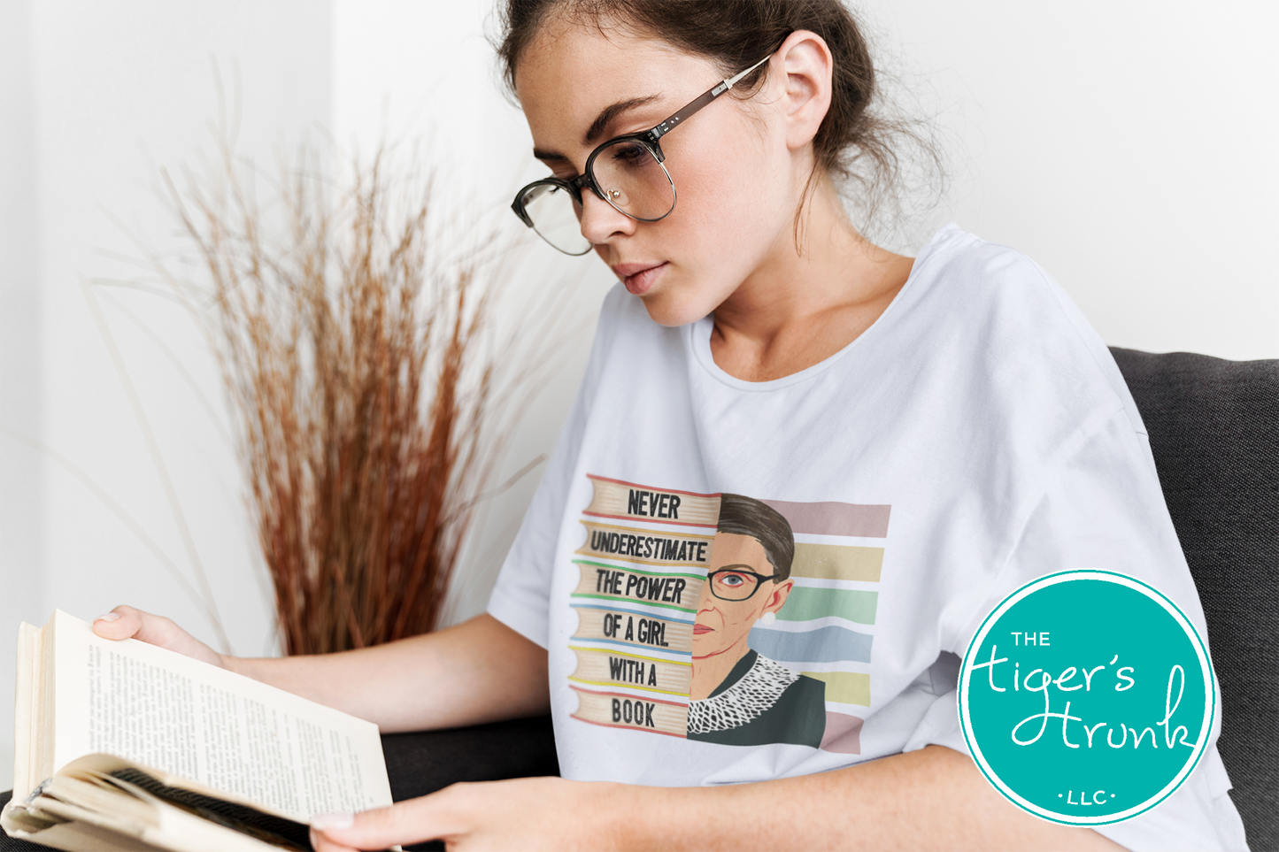 Woman reading a book wearing a t-shirt with a graphic design and 'The Tiger's Trunk' logo.