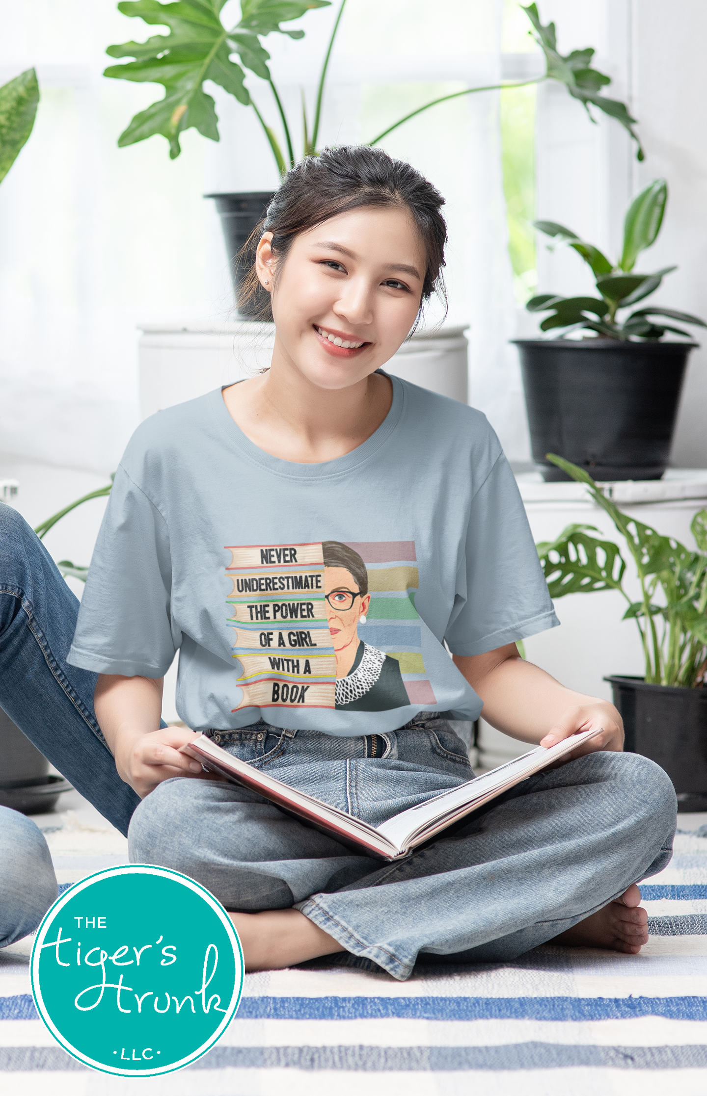 Woman sitting on the floor with a book, wearing a t-shirt with a graphic design, in a room with plants.