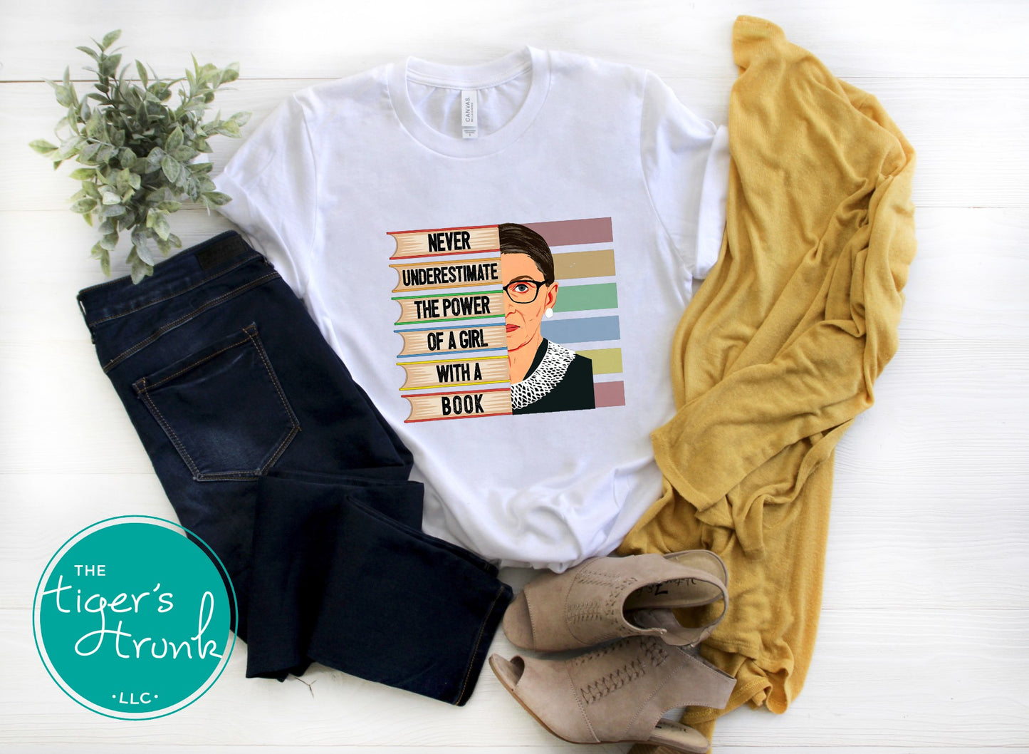 White t-shirt with graphic design and text, paired with jeans and a yellow sweater on a white surface.