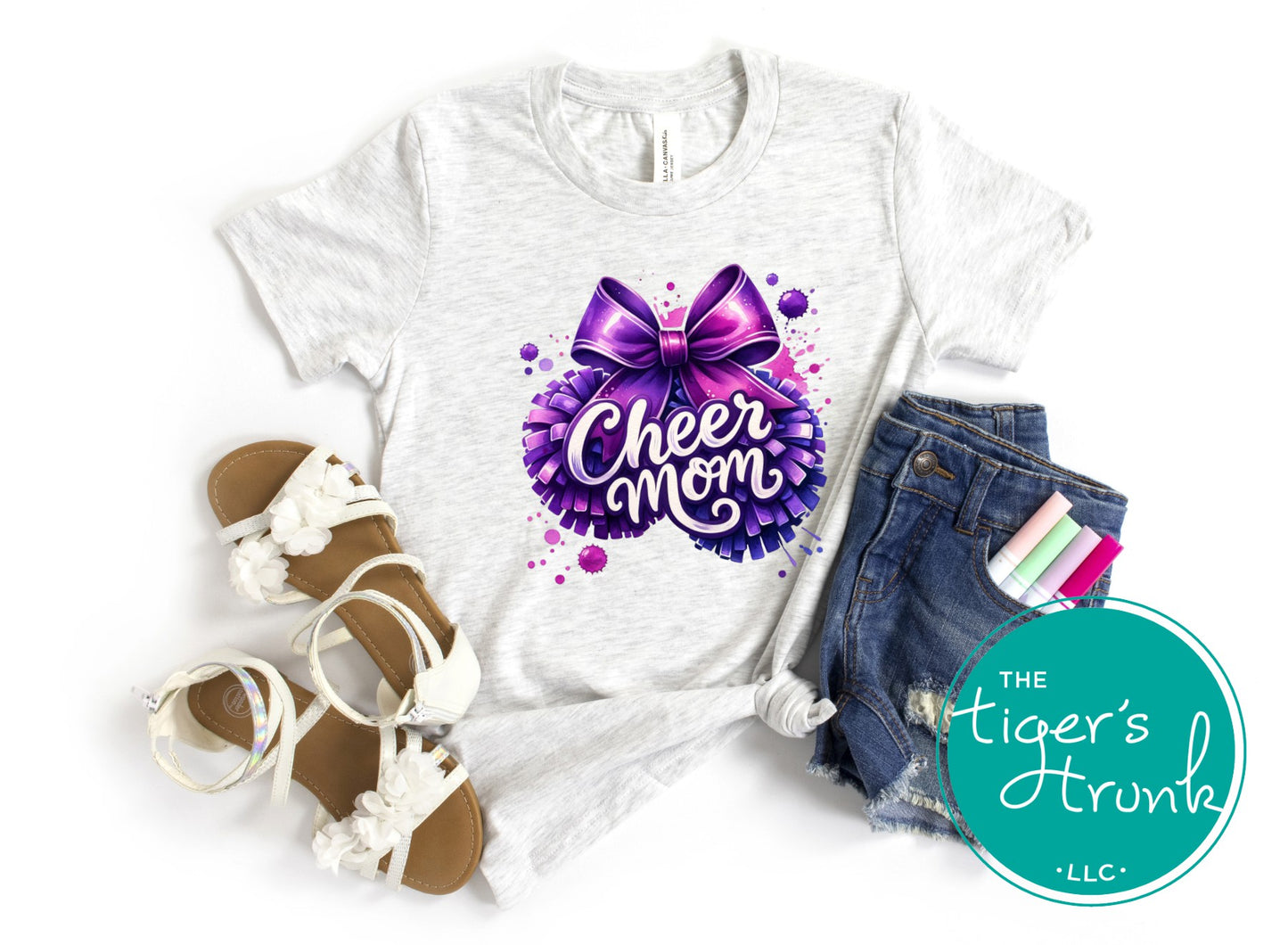 White t-shirt with 'Cheer Mom' design, sandals, shorts, and stationery on a white background with 'The Tiger's Trunk' logo.