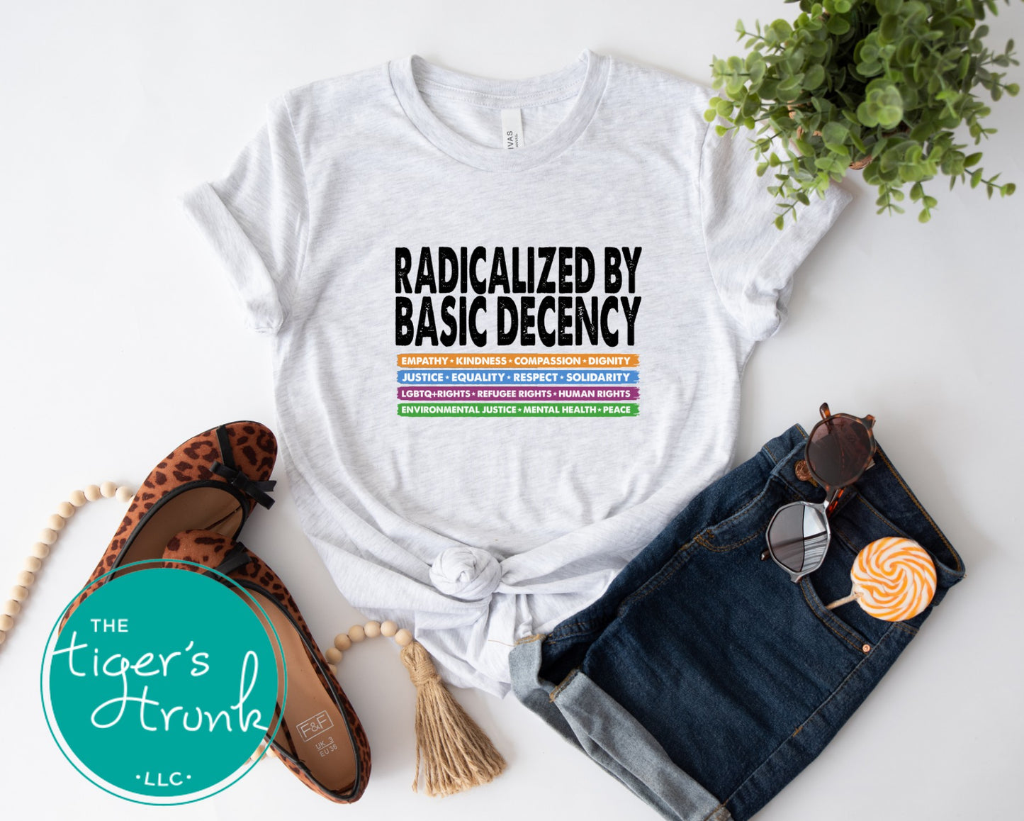 White t-shirt with text, denim shorts, flats, and sunglasses on a white background with 'The Tiger's Trunk' logo.