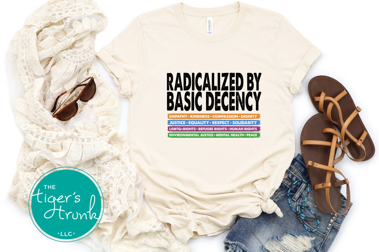 Beige t-shirt with text 'Radicalized by Basic Decency' on a white background, surrounded by scarf, sandals, and jeans.
