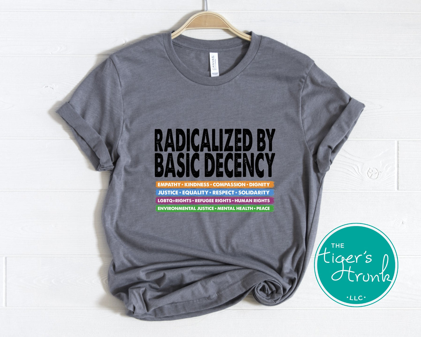 Gray t-shirt with text 'RADICALIZED BY BASIC DECENCY' on a white background, featuring the brand 'The Tiger's Trunk'.