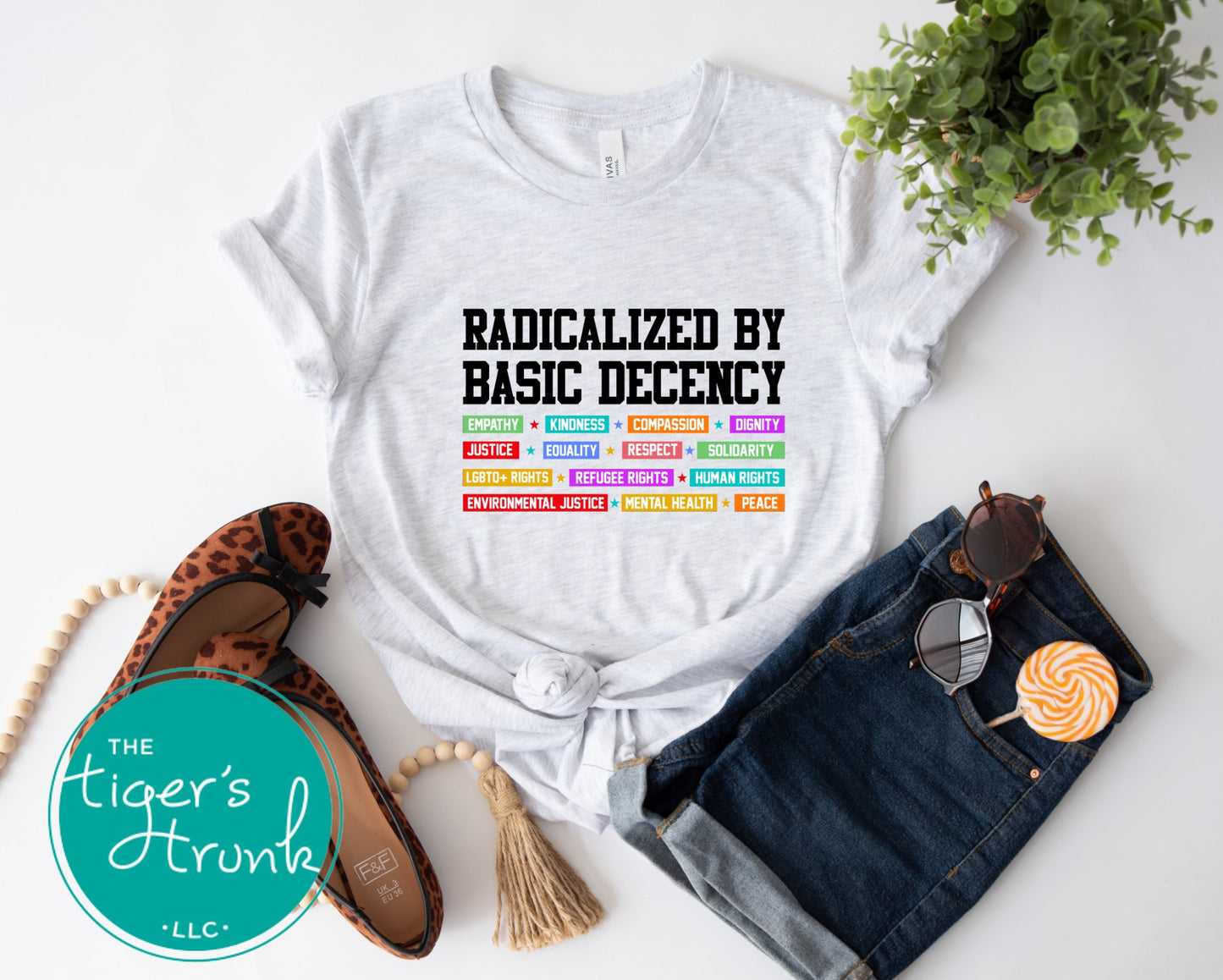 White t-shirt with text and colorful graphics, paired with denim shorts, flats, and sunglasses on a white background.