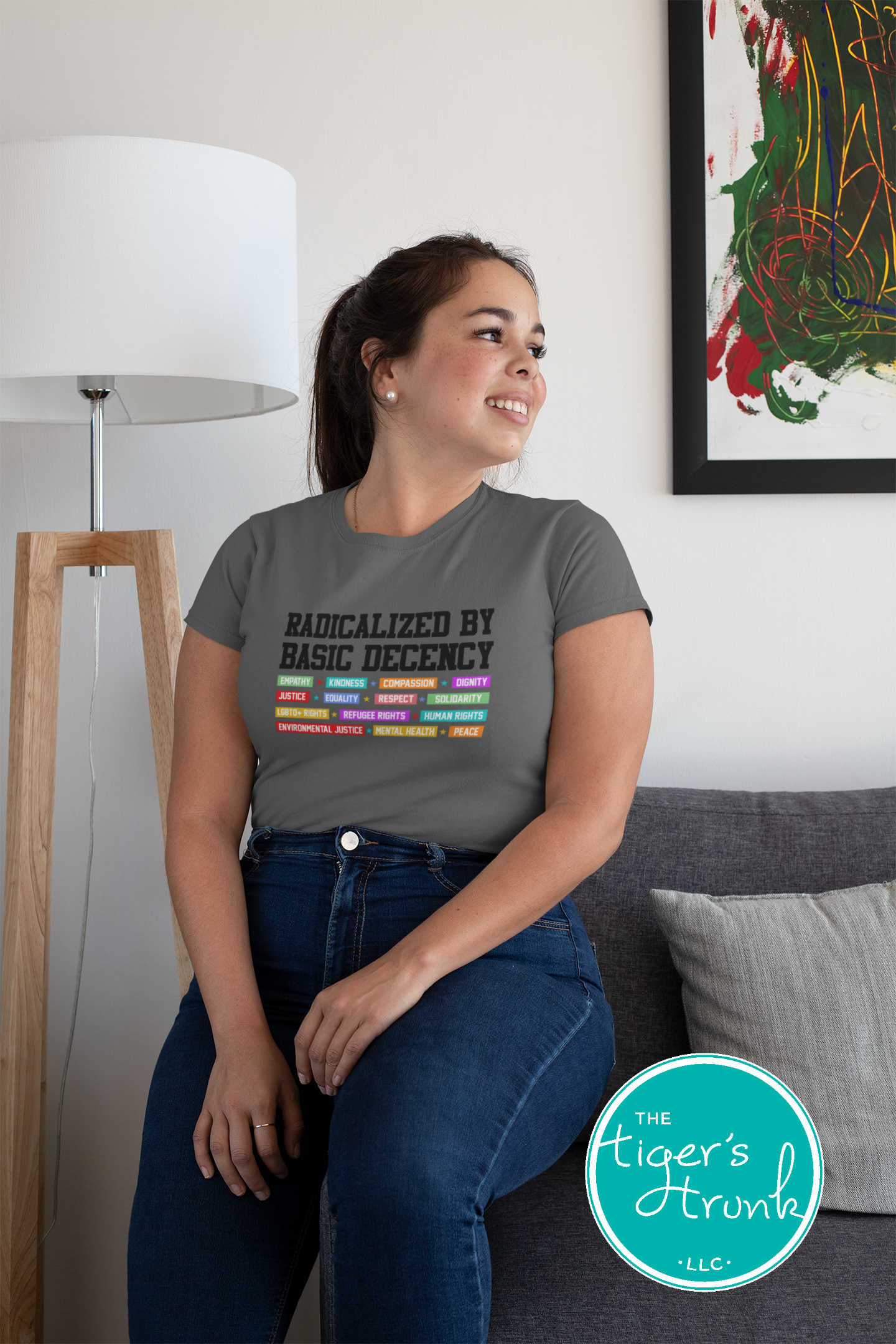 Woman wearing a gray t-shirt with colorful text design, sitting on a couch in a living room.