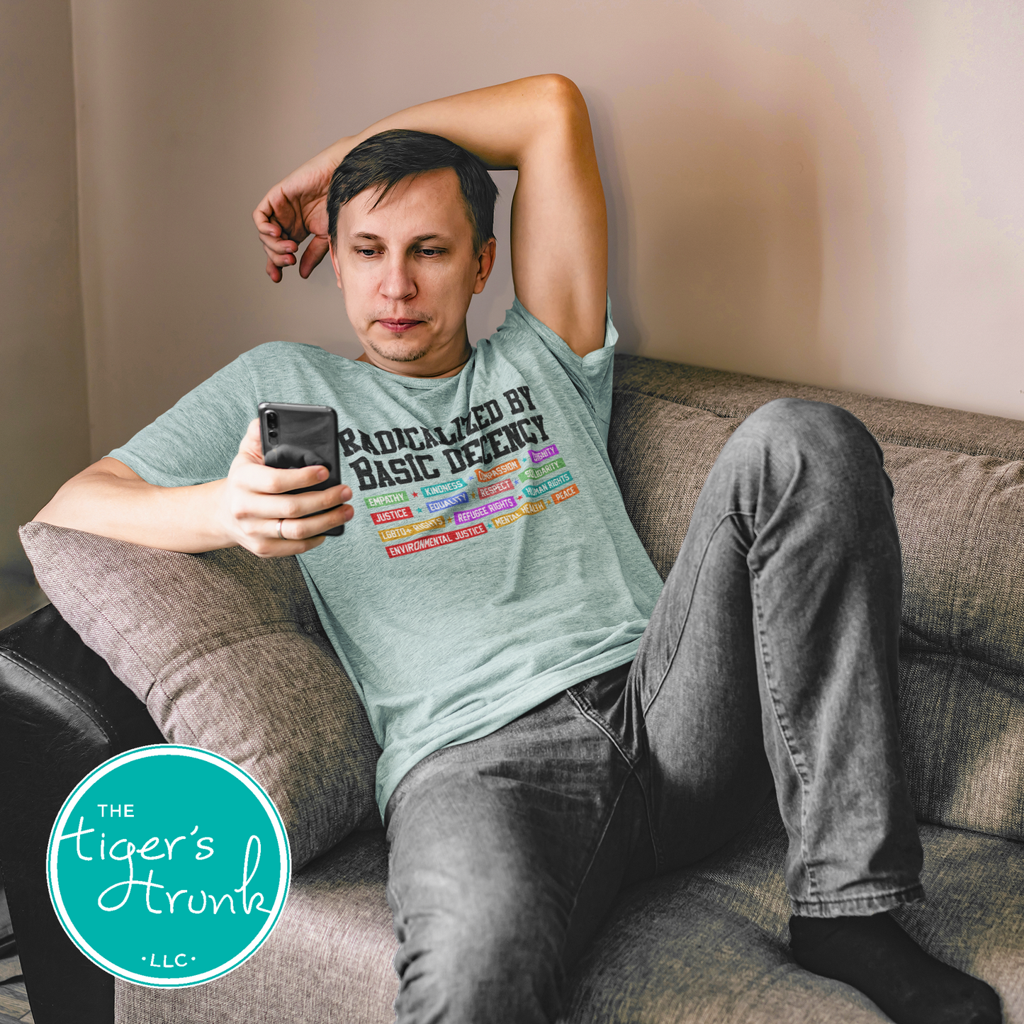 Man sitting on a couch using a phone with 'The Tiger's Trunk' logo in the corner.