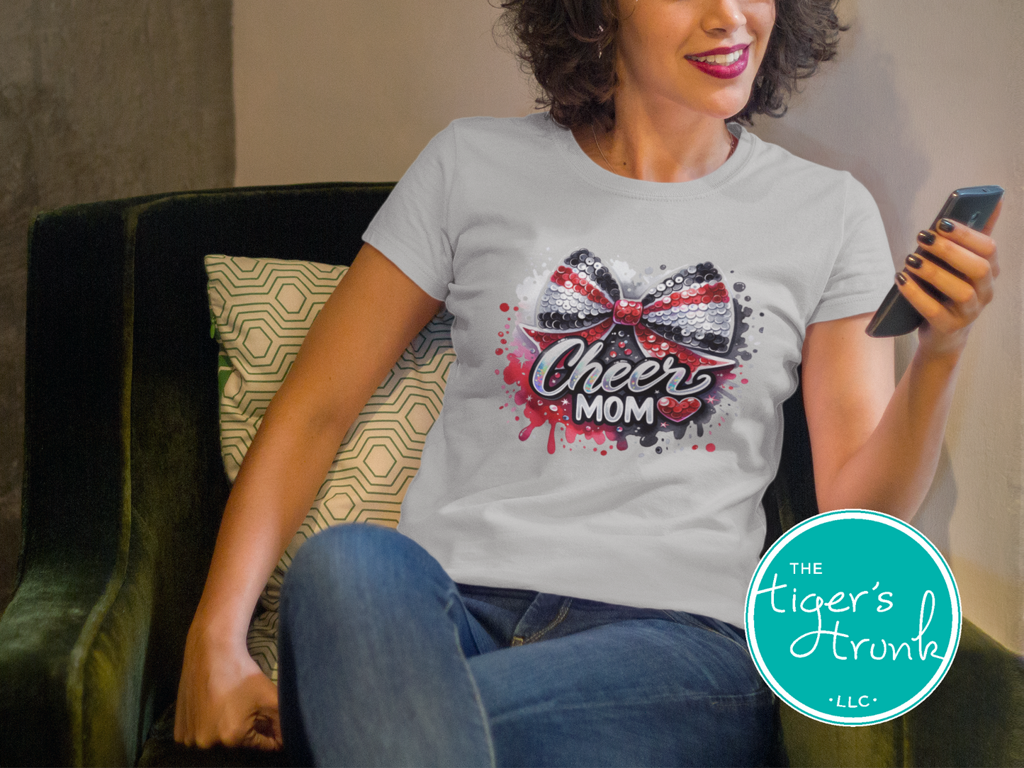 Woman wearing a 'Cheer Mom' t-shirt with a bow design, sitting on a couch.