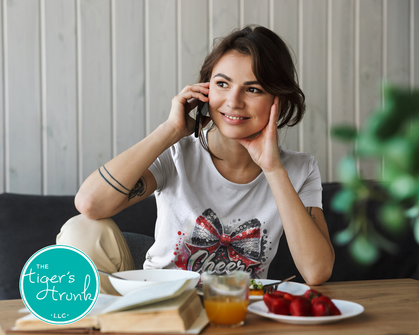 Woman sitting at a table with food and a phone, with 'The Tiger's Trunk' logo in the corner.